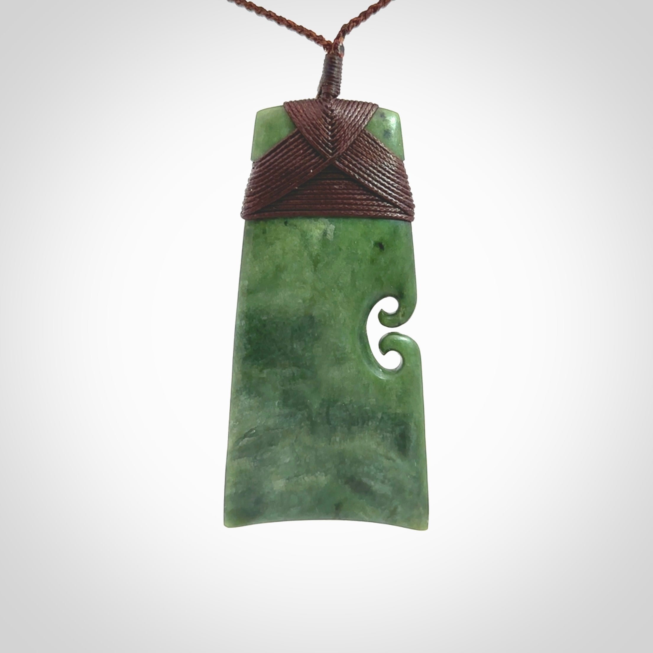 This is a lovely, one-off large green toki pendant hand made from a gorgeous New Zealand jade. It is finished in a matte sheen and is bound with a dark brown plaited cord. This toki has a koru carved into the side of the blade. This is a wonderful piece that is very attractive and will last a lifetime. Hand carved by Kyohei Noguchi.