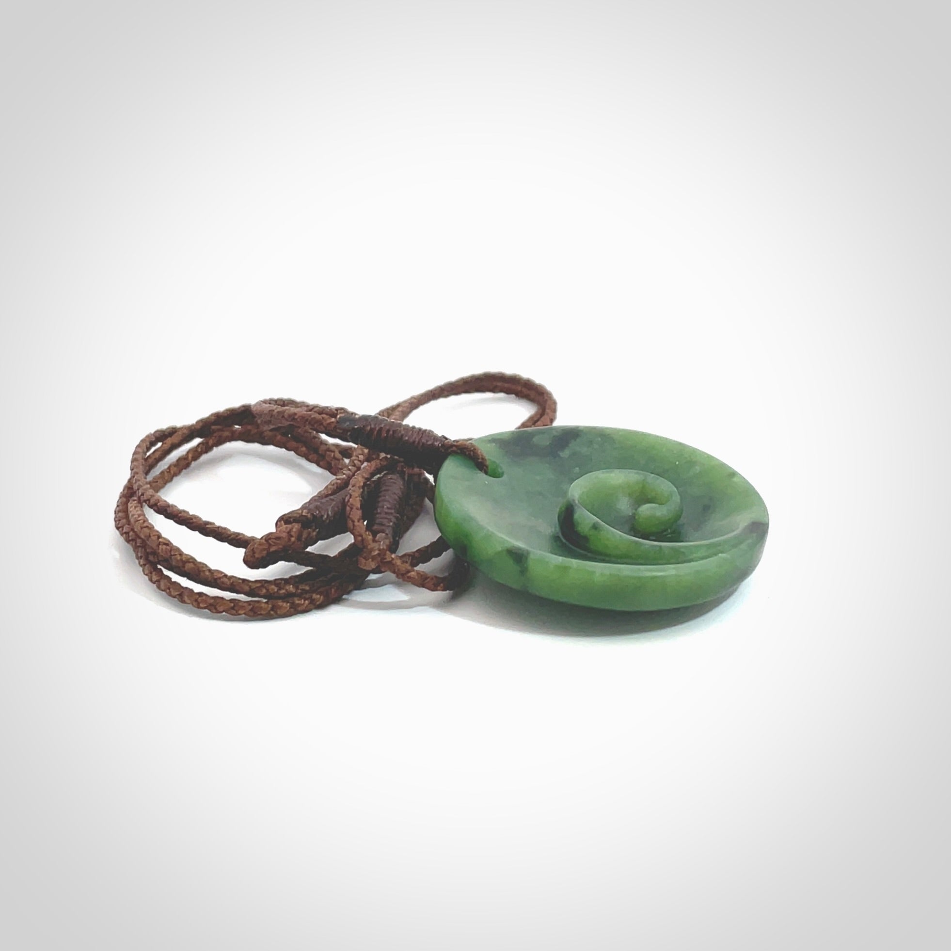 This pendant is a small sized and cupped koru necklace carved from a dark green piece of New Zealand Marsden Jade. Kyohei Noguchi carved this piece for us so the workmanship is outstanding. Handmade in New Zealand, a beautiful piece of jade jewellery. Provided with an adjustable brown cord and packaged in a woven kete pouch.