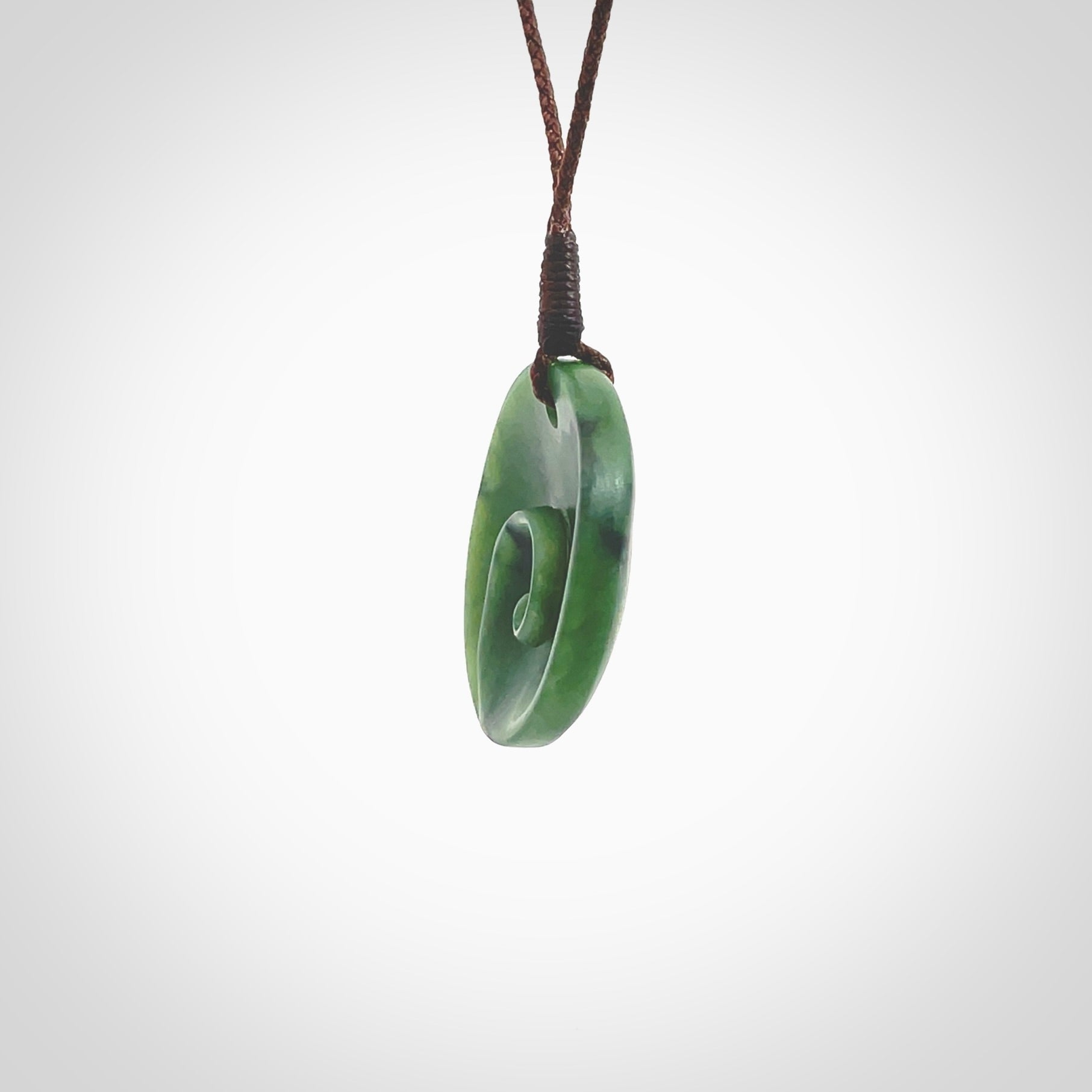 This pendant is a small sized and cupped koru necklace carved from a dark green piece of New Zealand Marsden Jade. Kyohei Noguchi carved this piece for us so the workmanship is outstanding. Handmade in New Zealand, a beautiful piece of jade jewellery. Provided with an adjustable brown cord and packaged in a woven kete pouch.