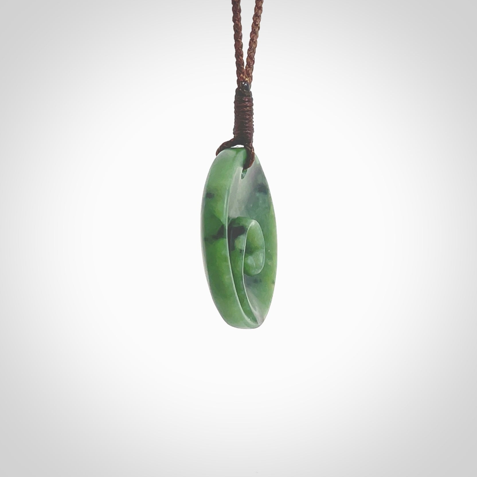 This pendant is a small sized and cupped koru necklace carved from a dark green piece of New Zealand Marsden Jade. Kyohei Noguchi carved this piece for us so the workmanship is outstanding. Handmade in New Zealand, a beautiful piece of jade jewellery. Provided with an adjustable brown cord and packaged in a woven kete pouch.