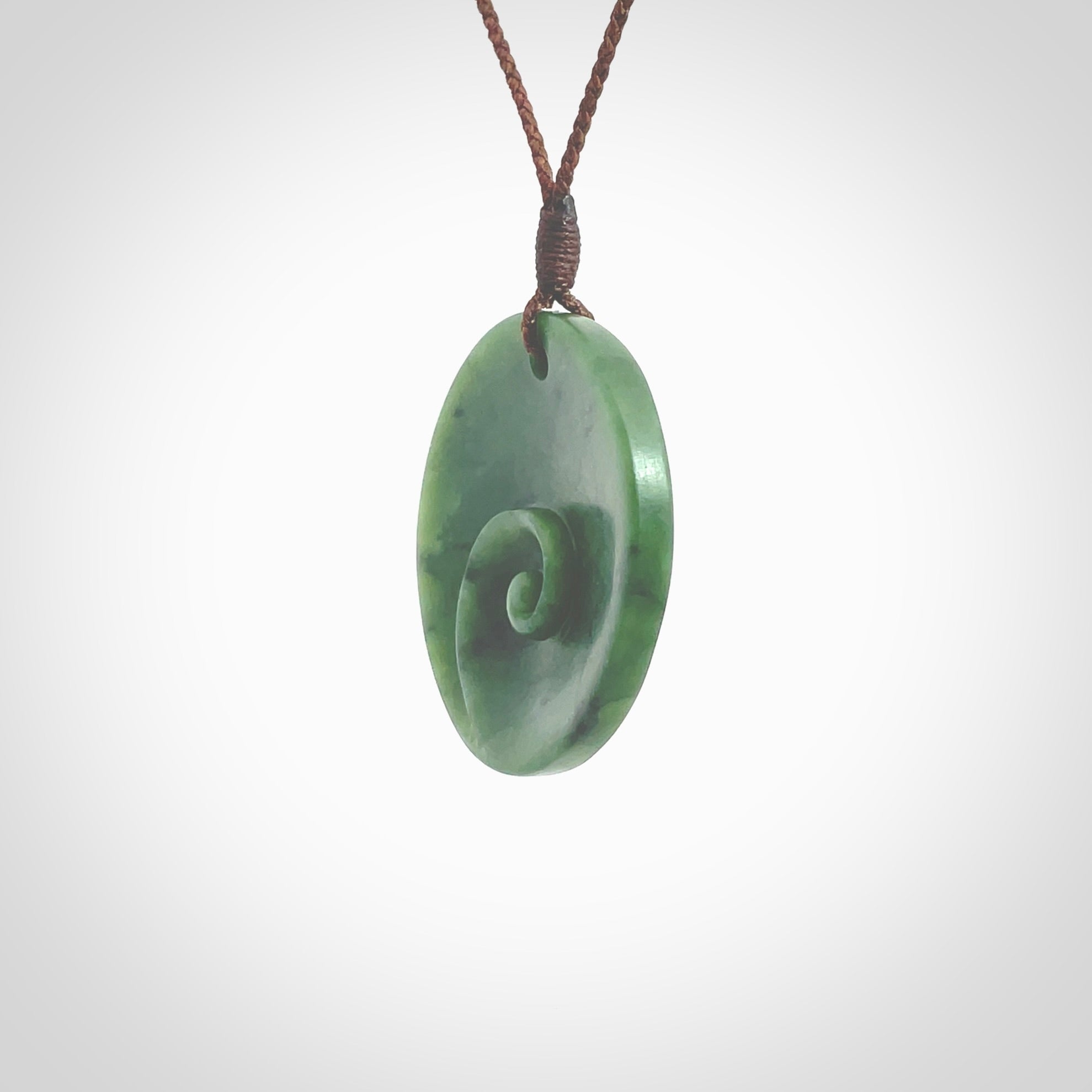 This pendant is a medium sized and cupped koru necklace carved from a lovely piece of New Zealand Jade. Kyohei Noguchi carved this piece for us so the workmanship is outstanding. Handmade in New Zealand, a beautiful piece of jade jewellery. Provided with an adjustable brown cord and packaged in a woven kete pouch.