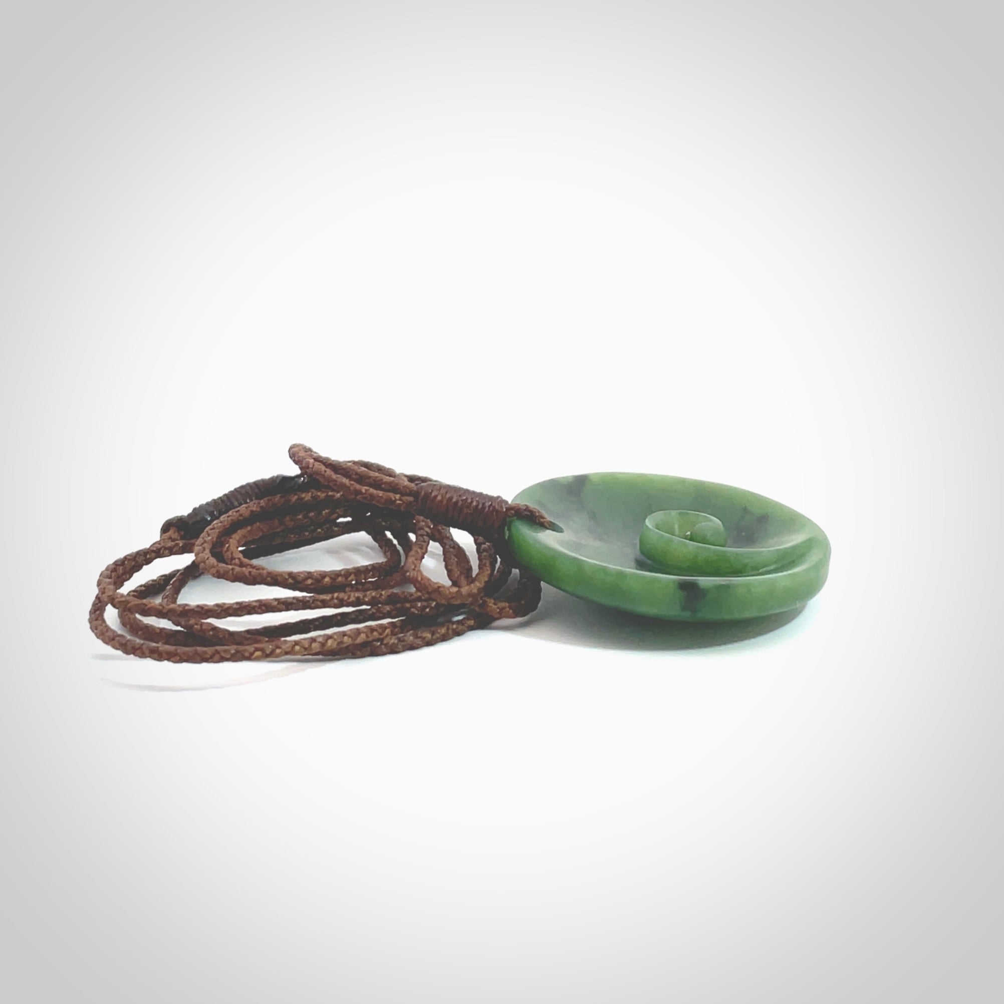 This pendant is a small sized and cupped koru necklace carved from a dark green piece of New Zealand Marsden Jade. Kyohei Noguchi carved this piece for us so the workmanship is outstanding. Handmade in New Zealand, a beautiful piece of jade jewellery. Provided with an adjustable brown cord and packaged in a woven kete pouch.