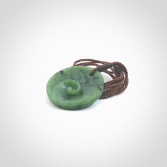 This pendant is a small sized and cupped koru necklace carved from a dark green piece of New Zealand Marsden Jade. Kyohei Noguchi carved this piece for us so the workmanship is outstanding. Handmade in New Zealand, a beautiful piece of jade jewellery. Provided with an adjustable brown cord and packaged in a woven kete pouch.