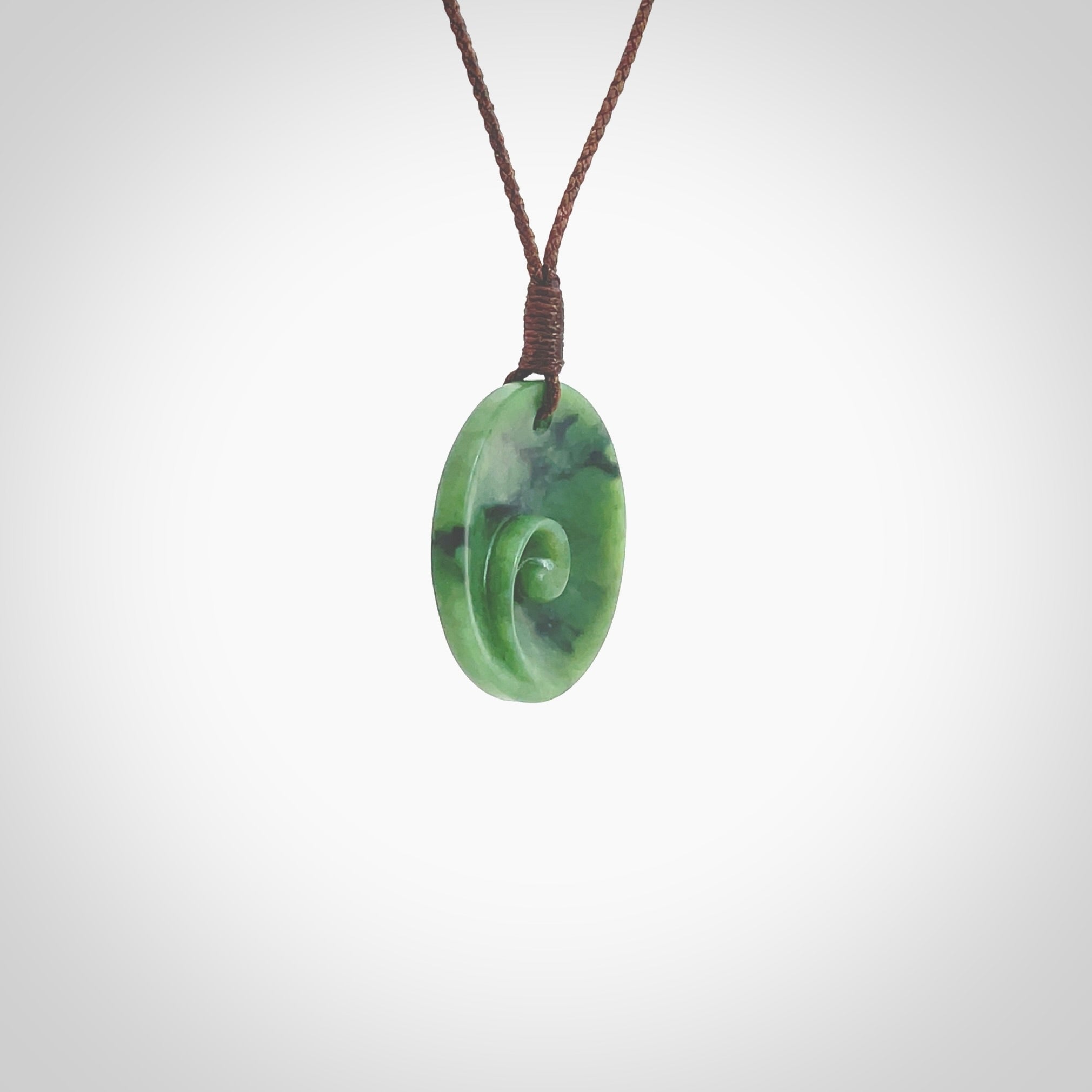 This pendant is a small sized and cupped koru necklace carved from a dark green piece of New Zealand Marsden Jade. Kyohei Noguchi carved this piece for us so the workmanship is outstanding. Handmade in New Zealand, a beautiful piece of jade jewellery. Provided with an adjustable brown cord and packaged in a woven kete pouch.