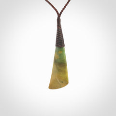 This photo shows a beautiful large sized flower jade drop. It is hand carved from a piece of New Zealand pounamu, with fascinating orange and green inclusions throughout the stone. We have this on a brown coloured, adjustable four plait cord. We ship this worldwide with an express courier service. Postage is free.