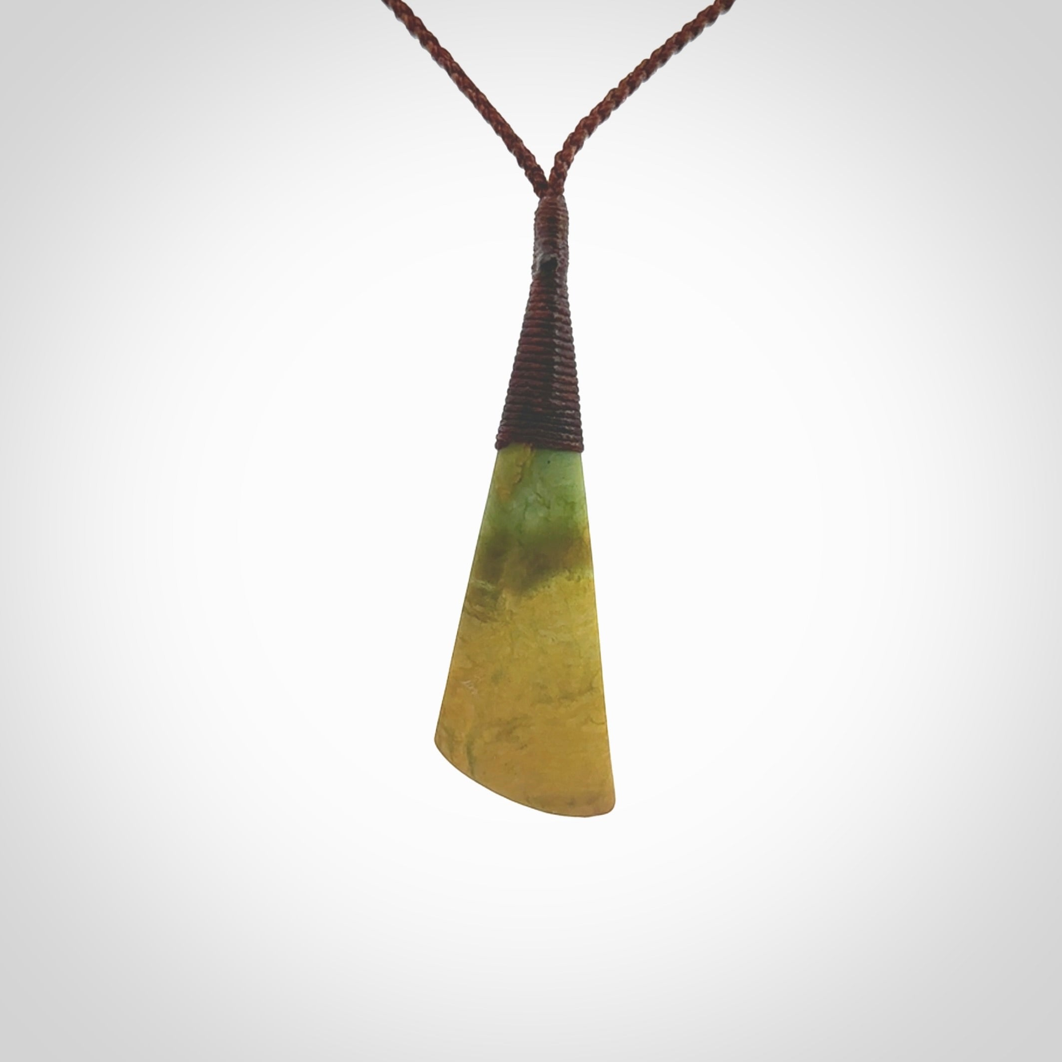 This photo shows a beautiful large sized flower jade drop. It is hand carved from a piece of New Zealand pounamu, with fascinating orange and green inclusions throughout the stone. We have this on a brown coloured, adjustable four plait cord. We ship this worldwide with an express courier service. Postage is free.