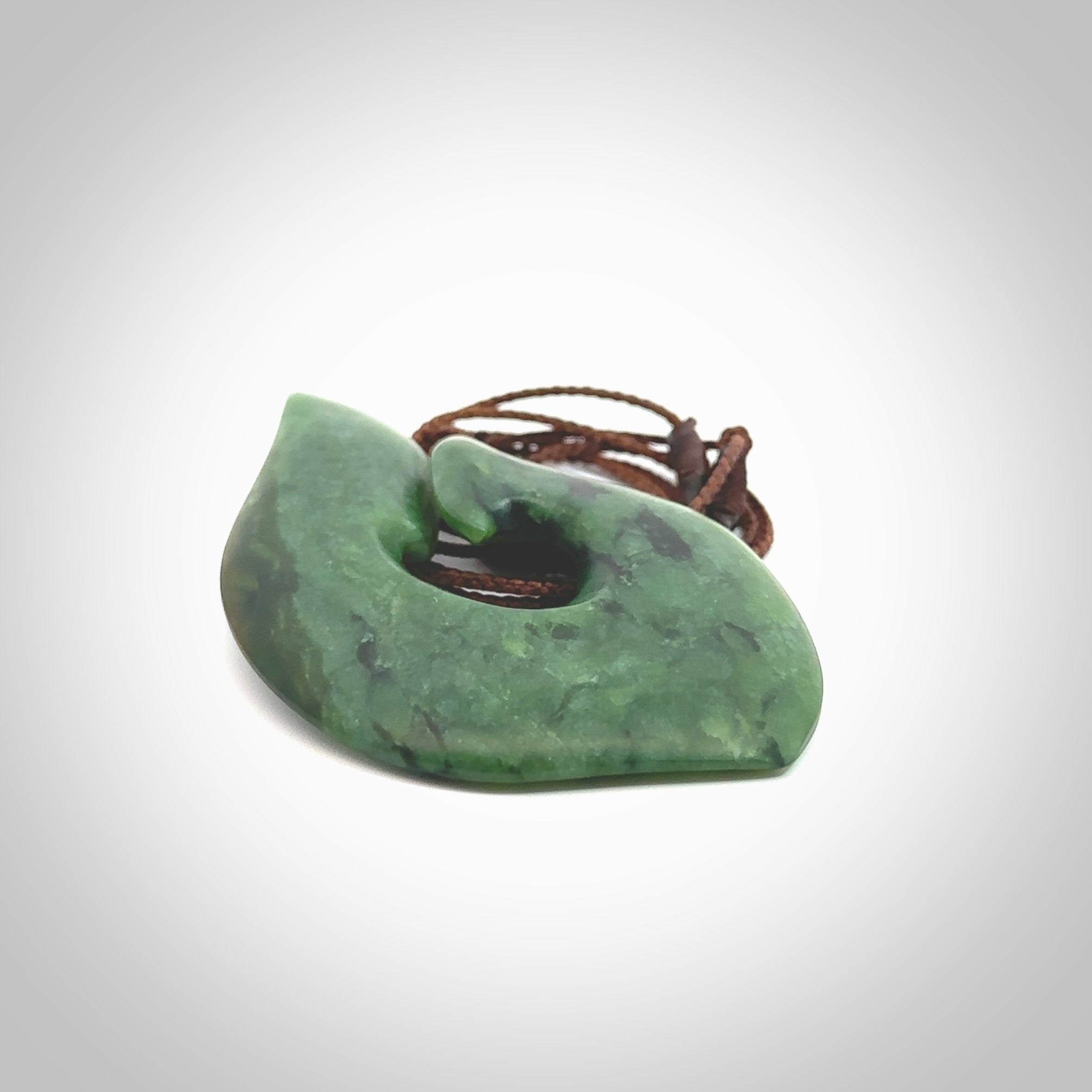 This photo shows a perfectly New Zealand jade hook pendant. It is hand carved from a deep green piece of New Zealand jade and is suspended on a brown four plait cord that is length adjustable. Hand carved Jade hook by Kyohei Noguchi.