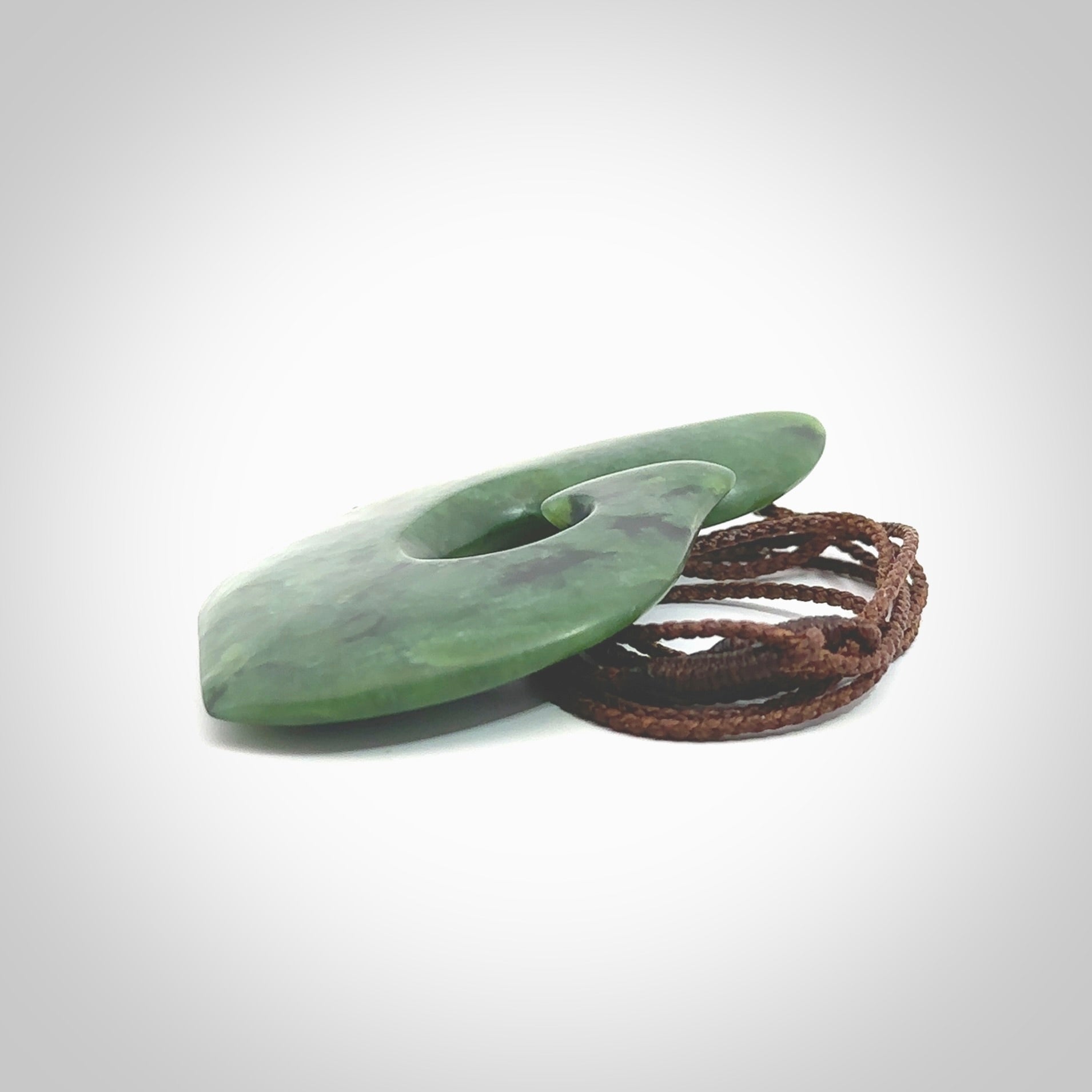 This photo shows a perfectly New Zealand jade hook pendant. It is hand carved from a deep green piece of New Zealand jade and is suspended on a brown four plait cord that is length adjustable. Hand carved Jade hook by Kyohei Noguchi.