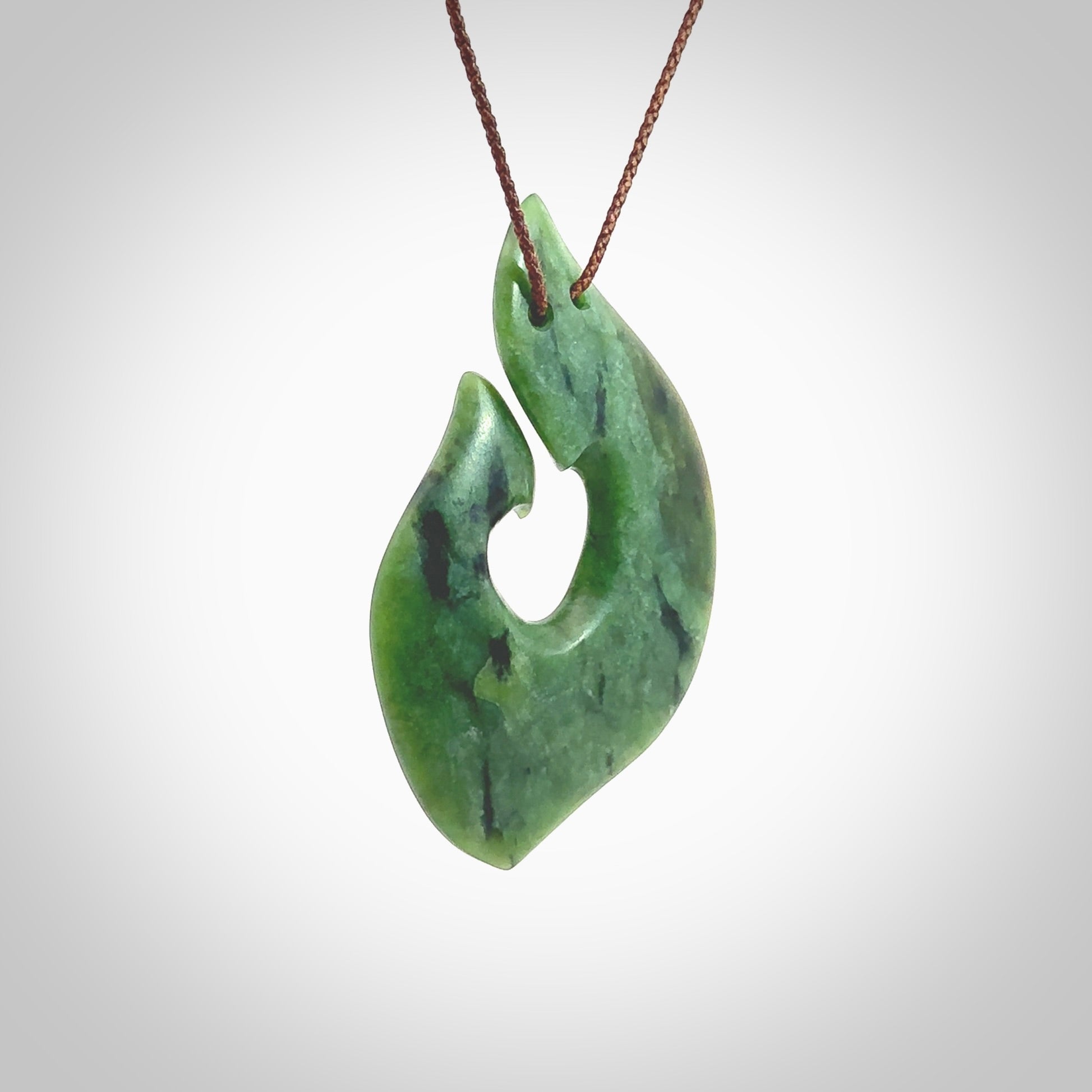 This photo shows a perfectly New Zealand jade hook pendant. It is hand carved from a deep green piece of New Zealand jade and is suspended on a brown four plait cord that is length adjustable. Hand carved Jade hook by Kyohei Noguchi.