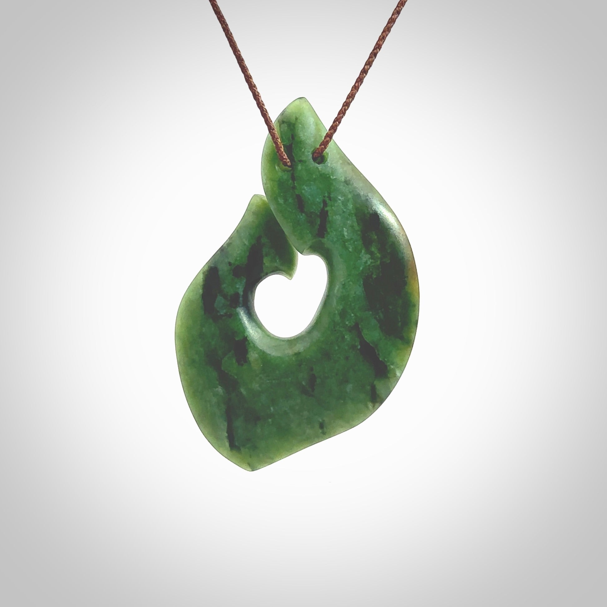 This photo shows a perfectly New Zealand jade hook pendant. It is hand carved from a deep green piece of New Zealand jade and is suspended on a brown four plait cord that is length adjustable. Hand carved Jade hook by Kyohei Noguchi.