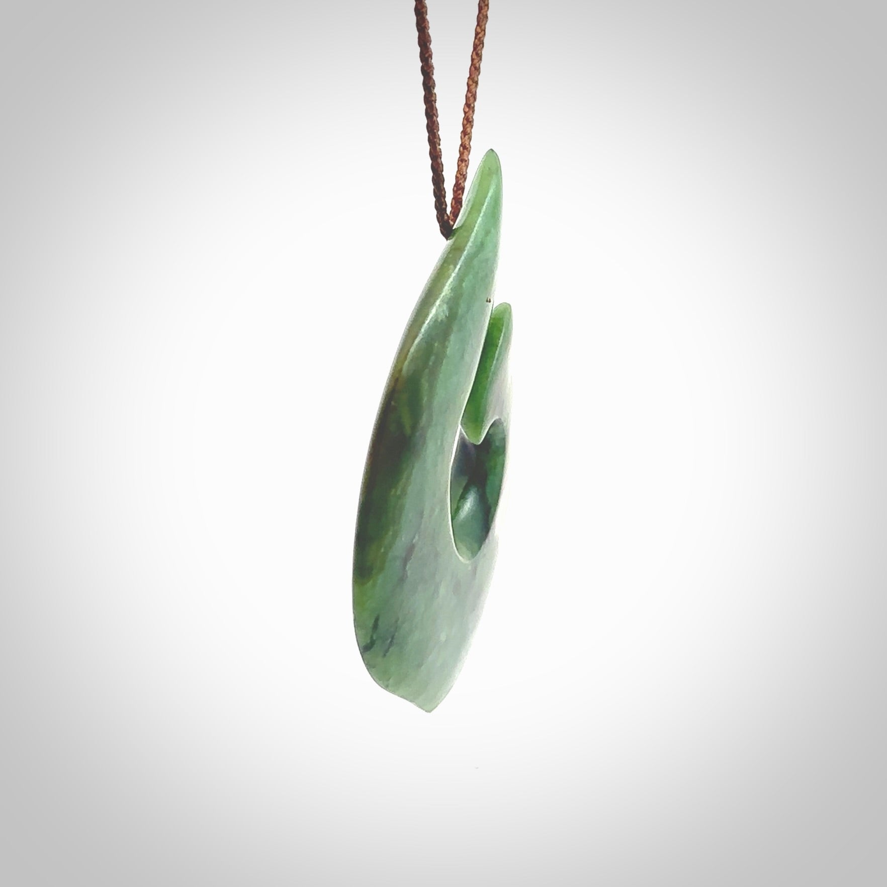 This photo shows a perfectly New Zealand jade hook pendant. It is hand carved from a deep green piece of New Zealand jade and is suspended on a brown four plait cord that is length adjustable. Hand carved Jade hook by Kyohei Noguchi.