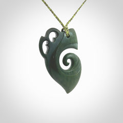 This photo shows a koru with a Kea head carved into the leading edge. The artist, Kerry Thompson, has carved this beautifully and he has polished parts of the carving to a high shine, and other parts he has left in a matte finish. The contrast is beautiful. The pendant is suspended from a plaited grass green/sage green cord which is adjustable.