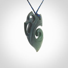 This photo shows a koru with a Owl head carved into the leading edge. The artist, Kerry Thompson, has carved this beautifully and he has polished parts of the carving to a high shine, and other parts he has left in a matte finish. The contrast is beautiful. The pendant is suspended from a plaited pacific blue/black cord which is adjustable.