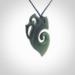 This photo shows a koru with a Owl head carved into the leading edge. The artist, Kerry Thompson, has carved this beautifully and he has polished parts of the carving to a high shine, and other parts he has left in a matte finish. The contrast is beautiful. The pendant is suspended from a plaited pacific blue/black cord which is adjustable.