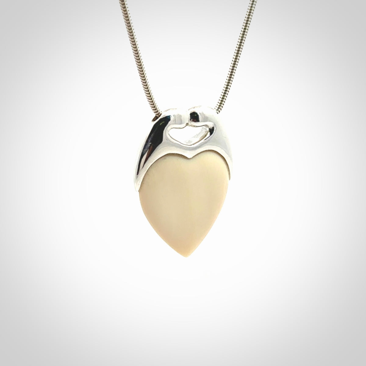 This picture shows a pendant that we have carved in a combination of sterling silver and woolly mammoth. It shows a symbolic kiss, with two heads coming together and both embracing a woolly mammoth heart. The necklace is a sterling silver chain.