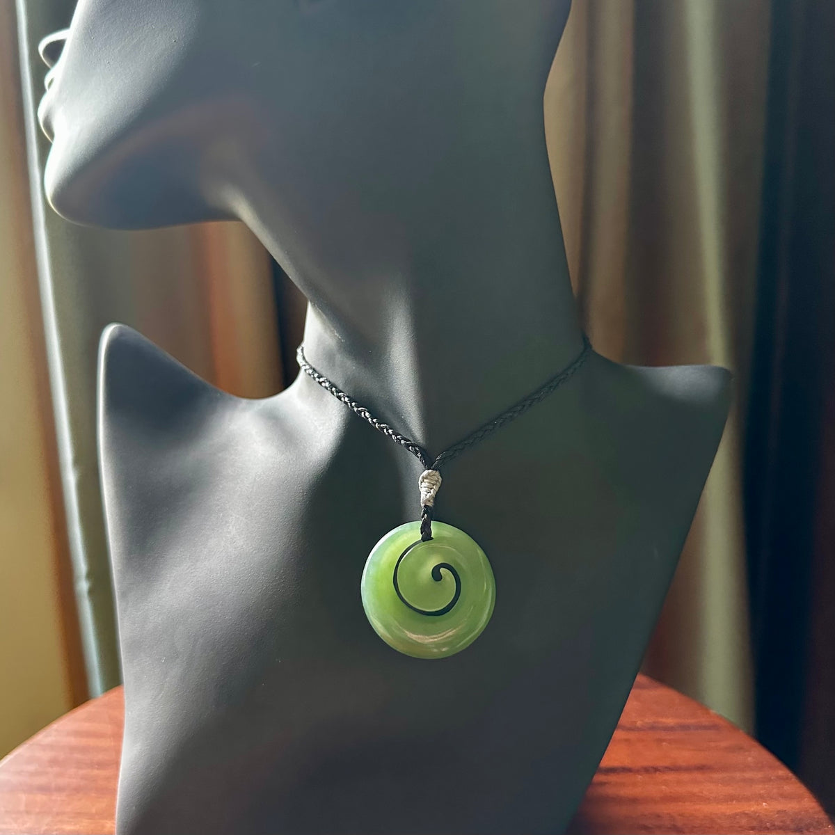 This picture shows a koru carving. A pendant carved from a lovely piece of New Zealand Inanga jade. We have suspended this necklace on a hand plaited cord in black and you can adjust its length so that you can position the pendant where it suits you best.