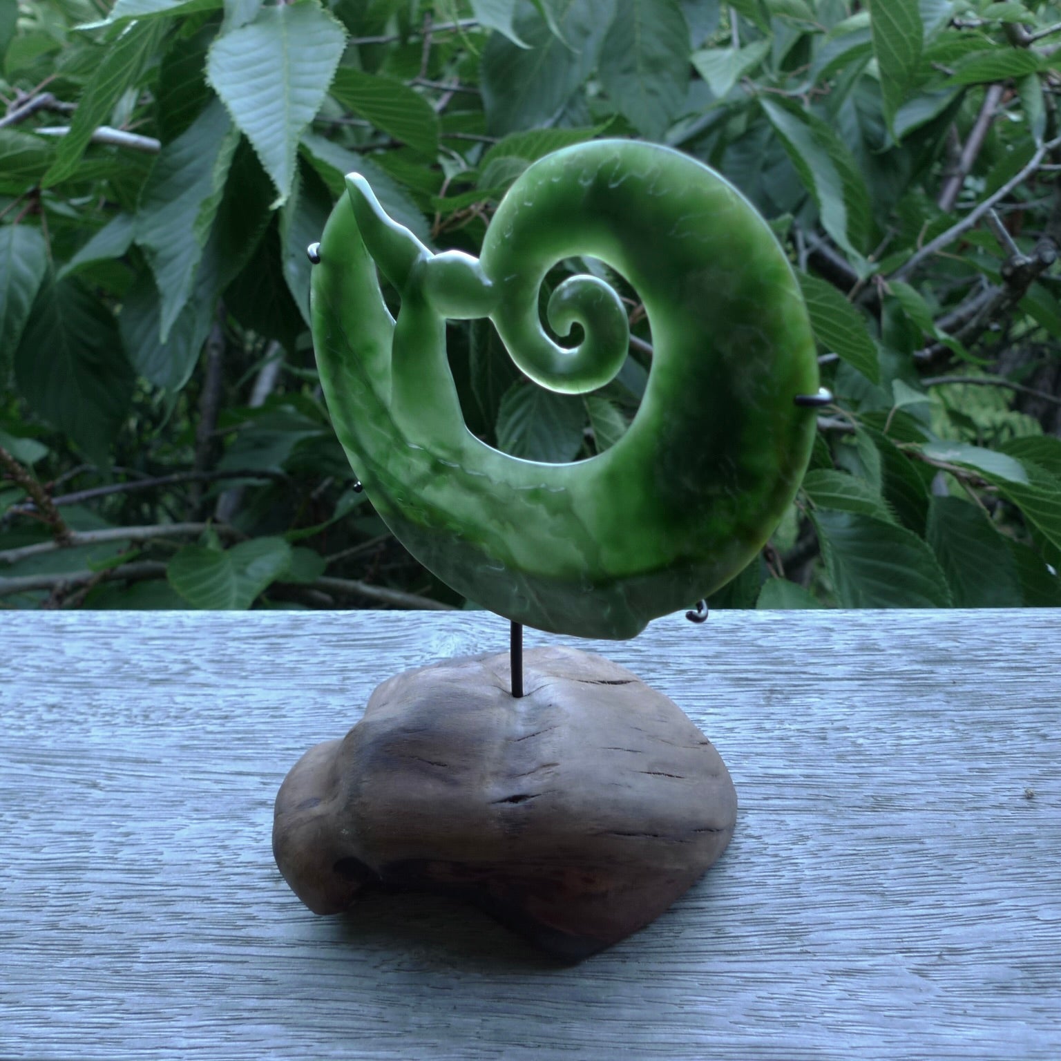 A photo of a New Zealand Jade whale tail in a wave sculpture with Rata Burr stand. This is a statement piece - hand crafted here in New Zealand by Ana Krakosky. Unique Art to display. Gifts for all lovers of hand made sculptures.