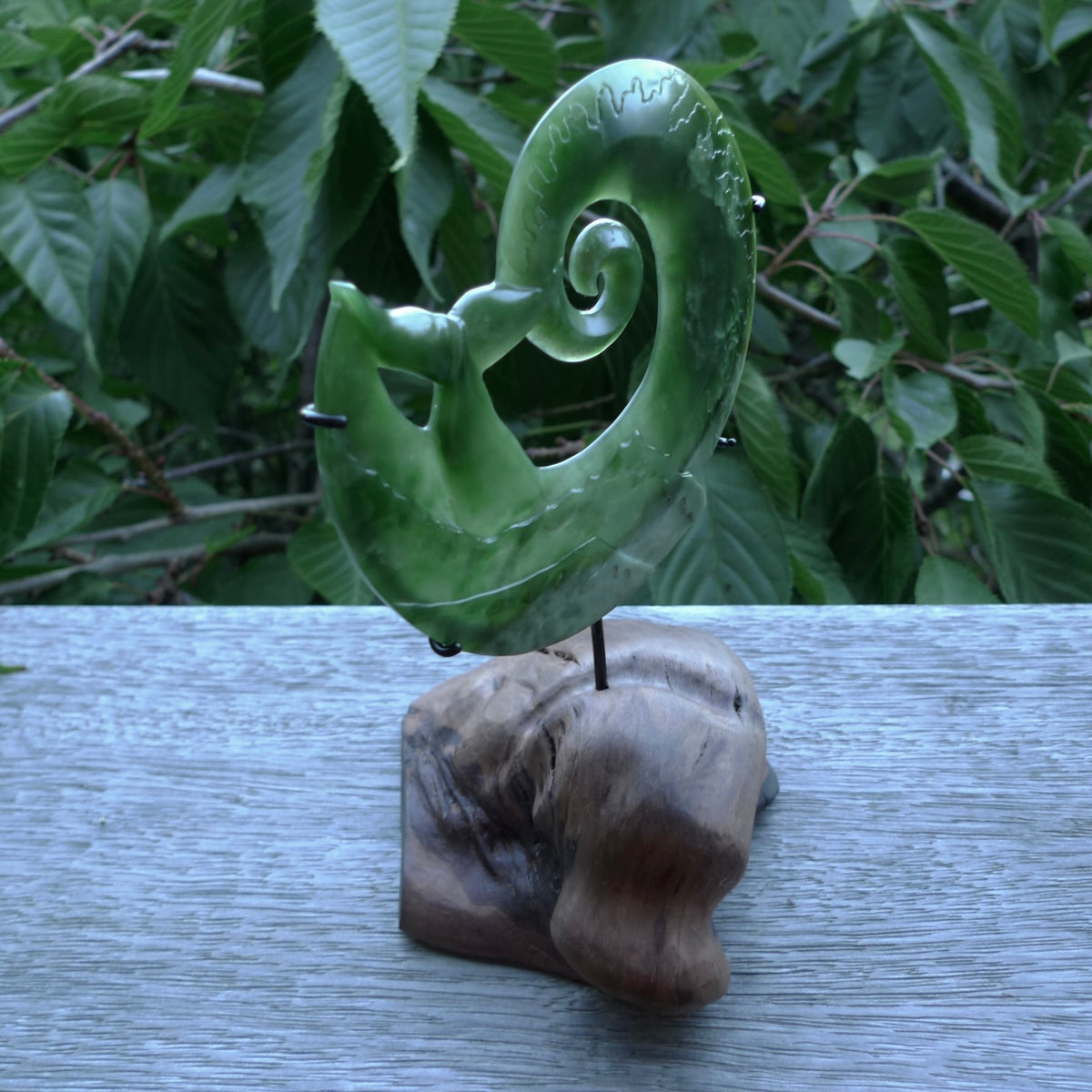 A photo of a New Zealand Jade whale tail in a wave sculpture with Rata Burr stand. This is a statement piece - hand crafted here in New Zealand by Ana Krakosky. Unique Art to display. Gifts for all lovers of hand made sculptures.