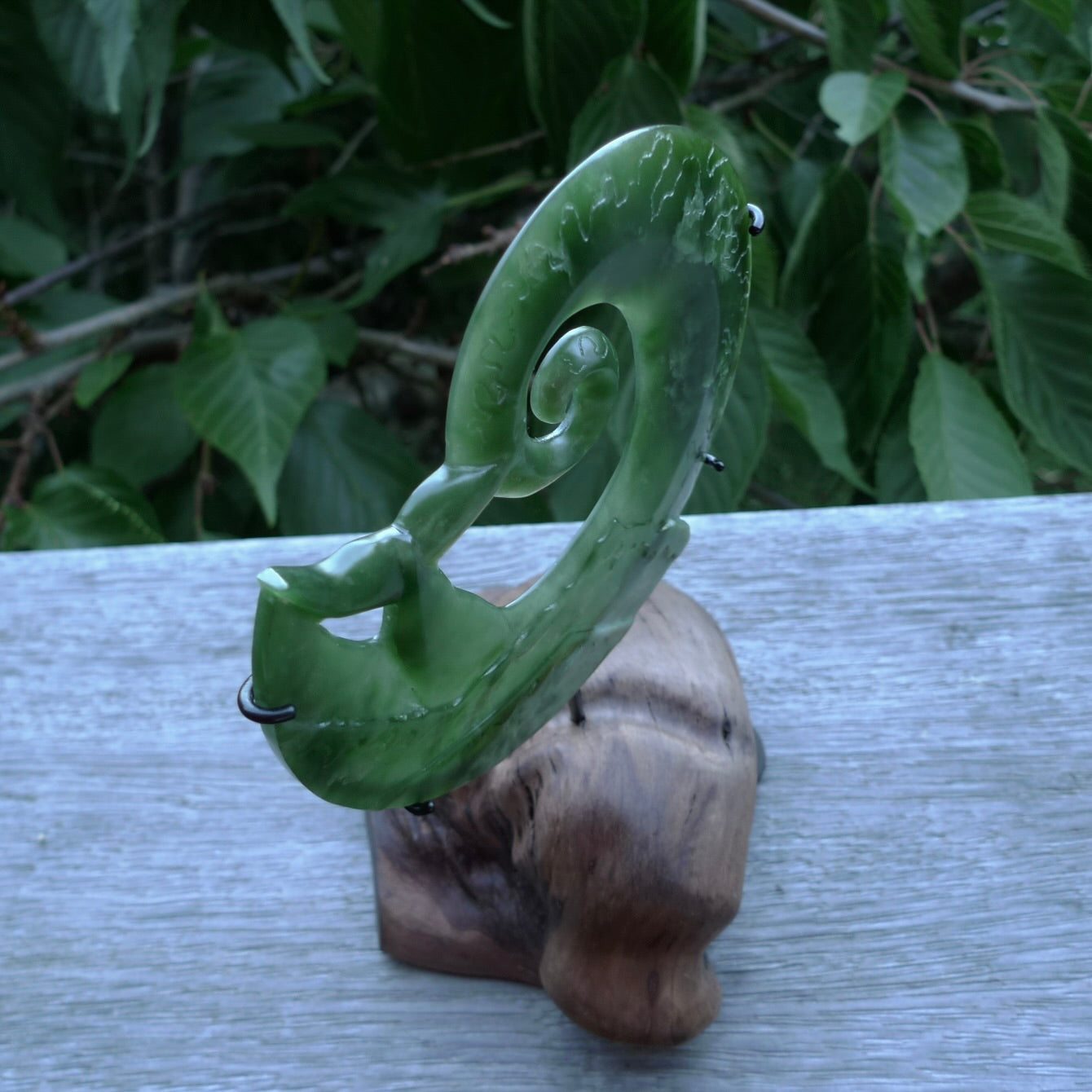 A photo of a New Zealand Jade whale tail in a wave sculpture with Rata Burr stand. This is a statement piece - hand crafted here in New Zealand by Ana Krakosky. Unique Art to display. Gifts for all lovers of hand made sculptures.