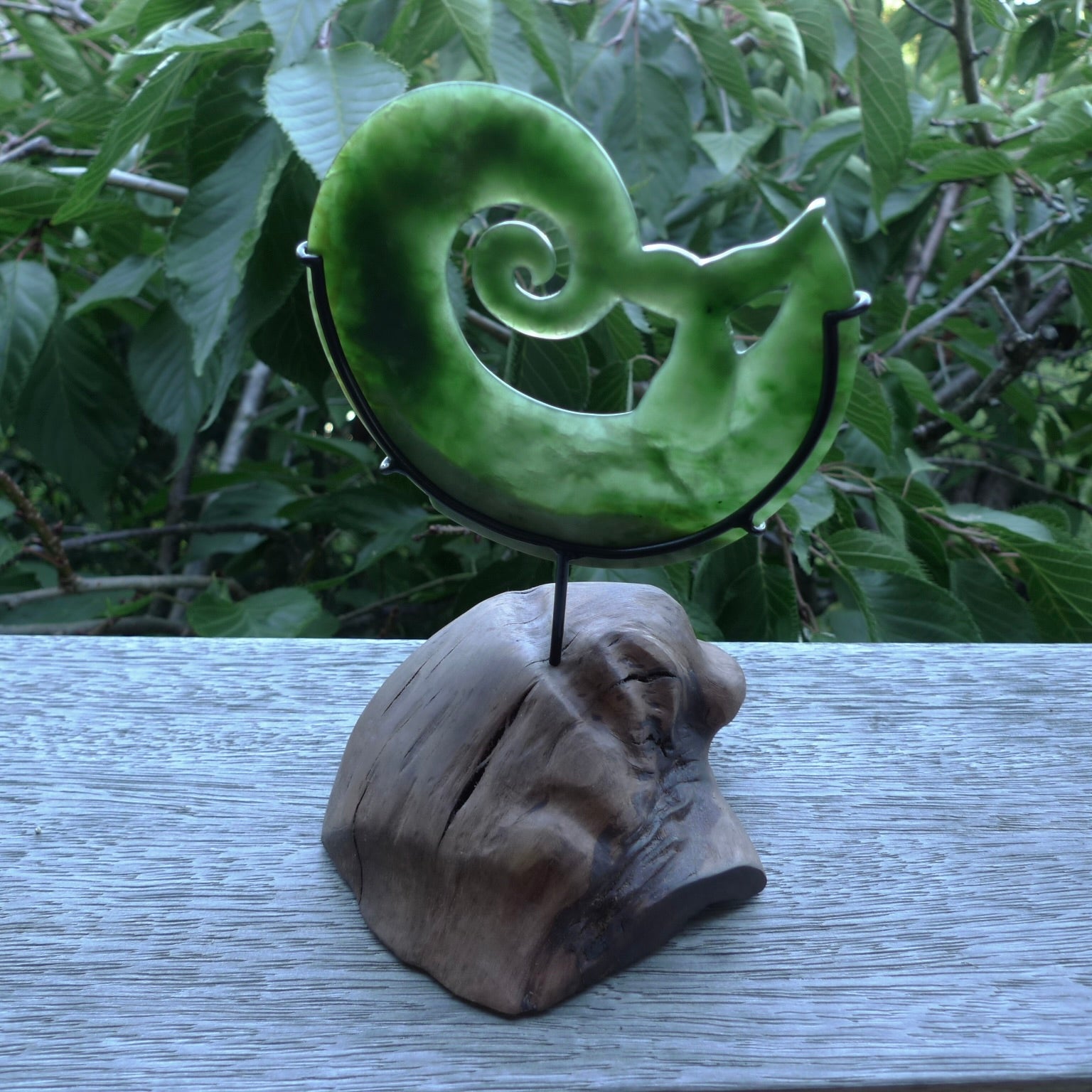 A photo of a New Zealand Jade whale tail in a wave sculpture with Rata Burr stand. This is a statement piece - hand crafted here in New Zealand by Ana Krakosky. Unique Art to display. Gifts for all lovers of hand made sculptures.