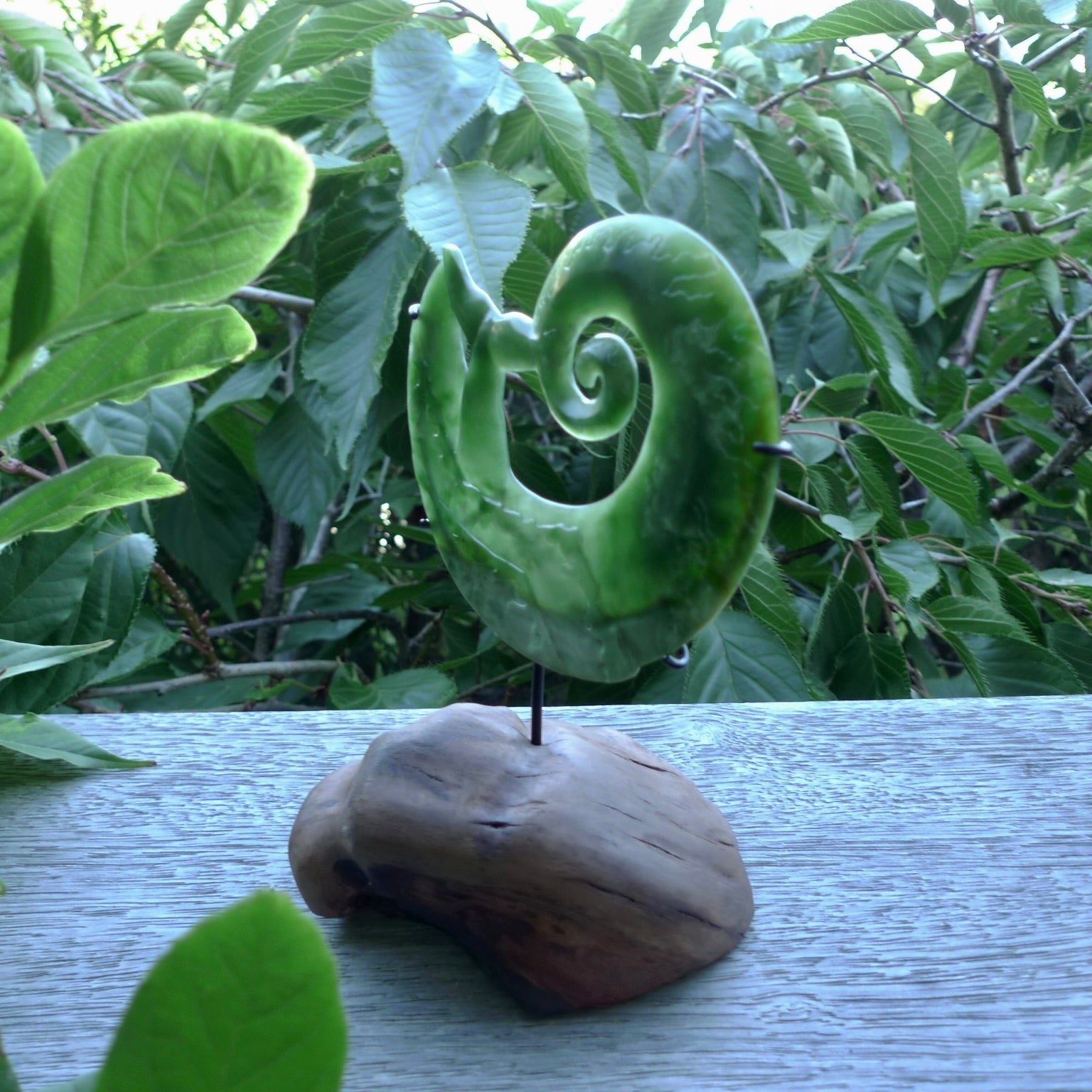 A photo of a New Zealand Jade whale tail in a wave sculpture with Rata Burr stand. This is a statement piece - hand crafted here in New Zealand by Ana Krakosky. Unique Art to display. Gifts for all lovers of hand made sculptures.