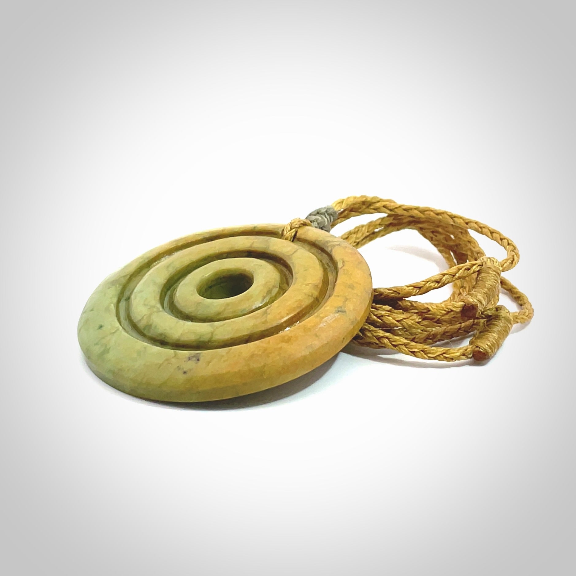 This picture shows a hand carved disc pendant made from a bright orange and green coloured flower jade. The front face is a unique design and the back is flat. It is provided with an adjustable sahara tan cord.