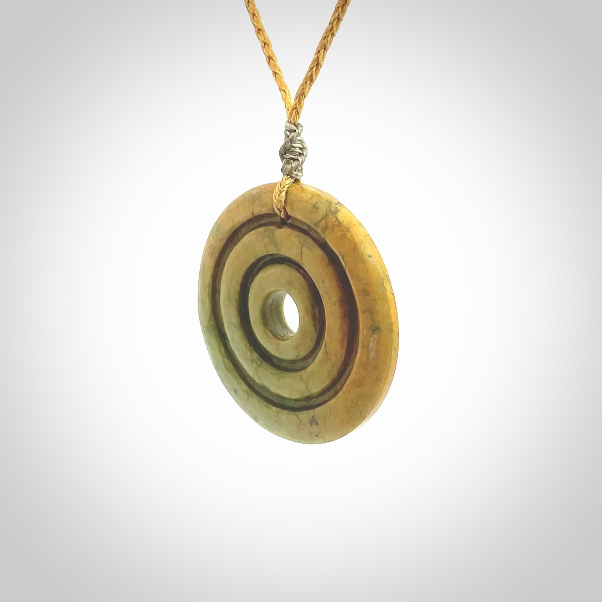 This picture shows a hand carved disc pendant made from a bright orange and green coloured flower jade. The front face is a unique design and the back is flat. It is provided with an adjustable sahara tan cord.