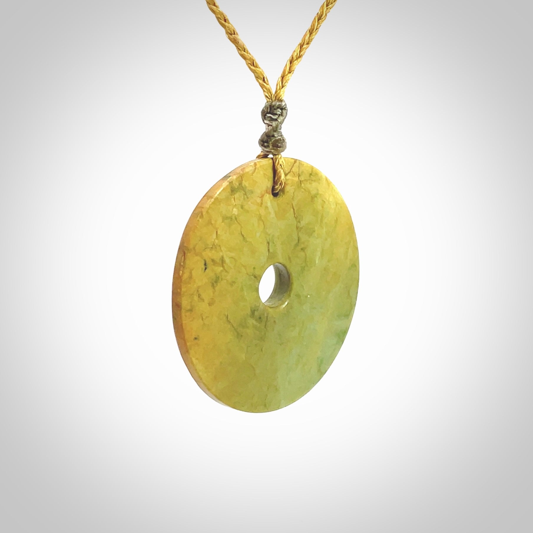 This picture shows a hand carved disc pendant made from a bright orange and green coloured flower jade. The front face is a unique design and the back is flat. It is provided with an adjustable sahara tan cord.