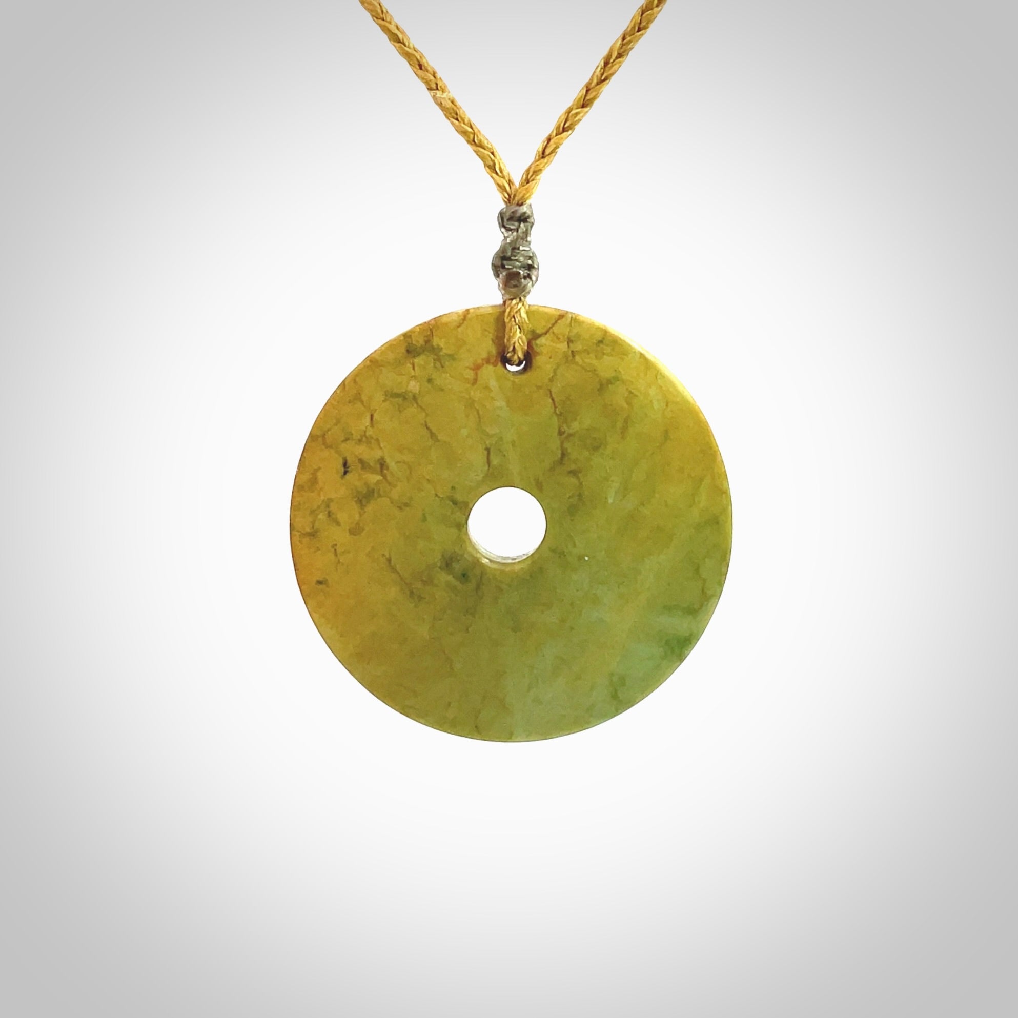 This picture shows a hand carved disc pendant made from a bright orange and green coloured flower jade. The front face is a unique design and the back is flat. It is provided with an adjustable sahara tan cord.