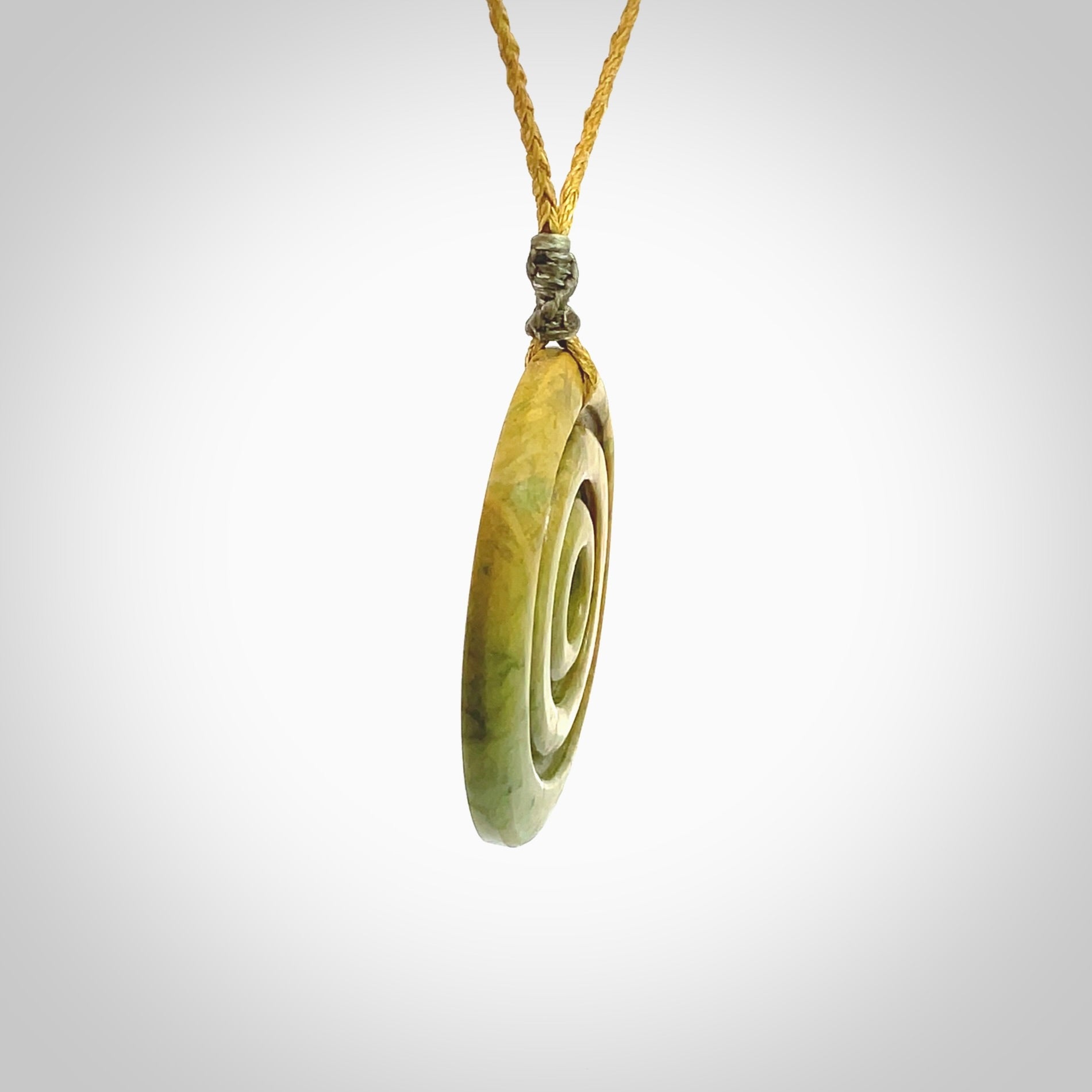 This picture shows a hand carved disc pendant made from a bright orange and green coloured flower jade. The front face is a unique design and the back is flat. It is provided with an adjustable sahara tan cord.