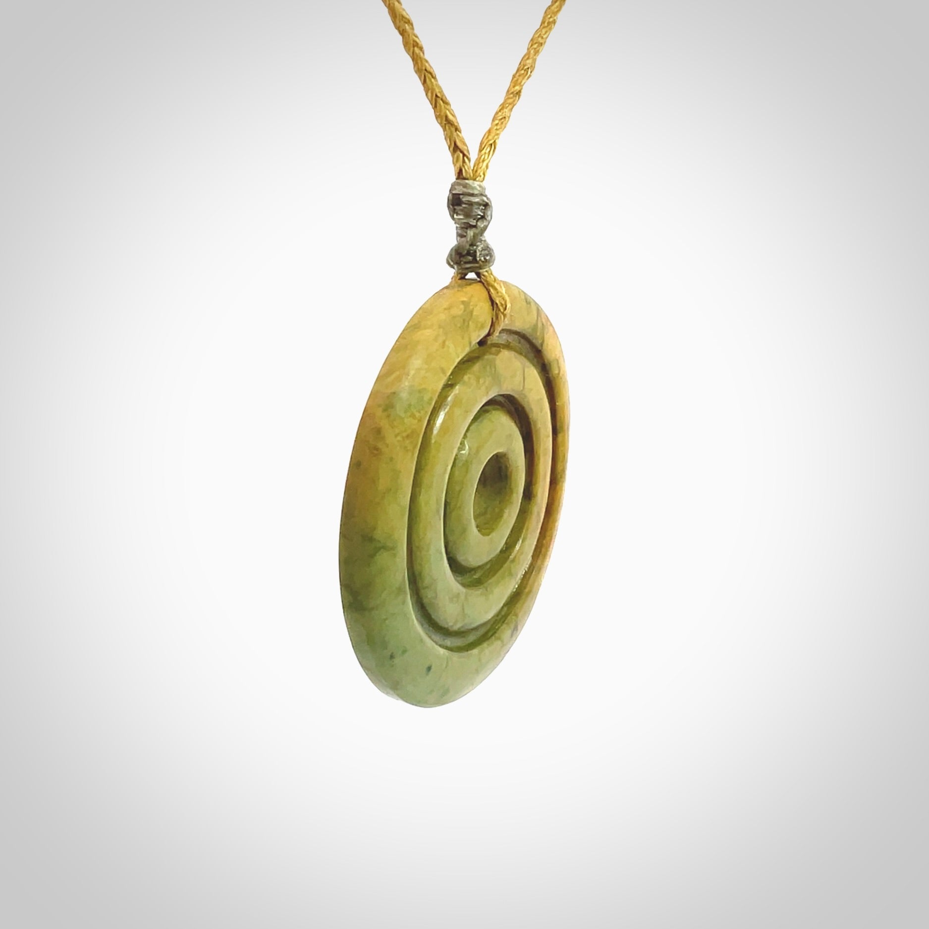 This picture shows a hand carved disc pendant made from a bright orange and green coloured flower jade. The front face is a unique design and the back is flat. It is provided with an adjustable sahara tan cord.