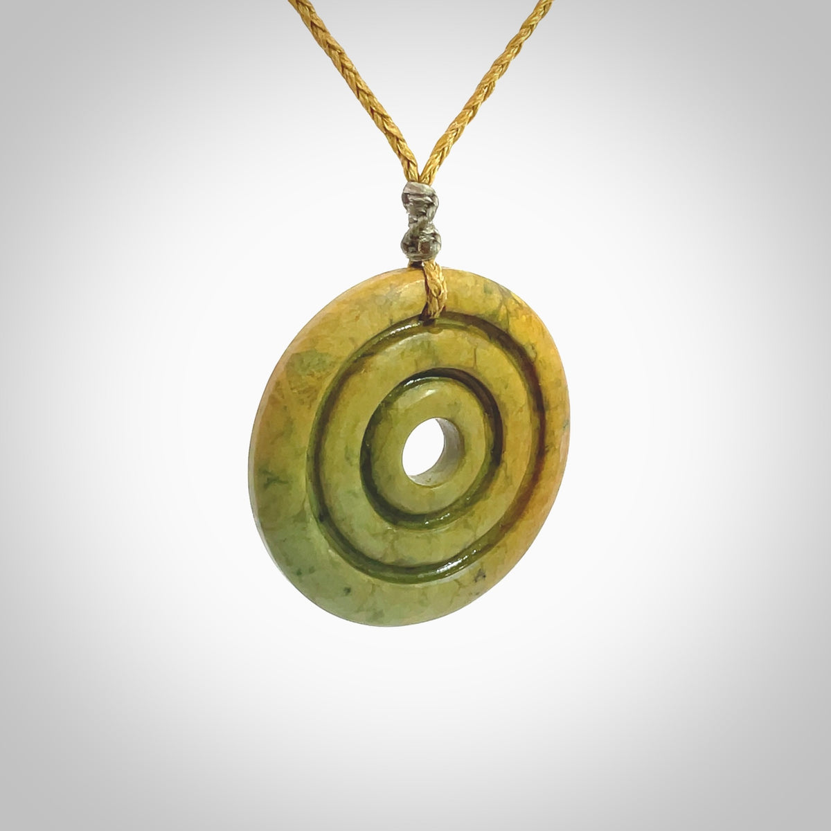 This picture shows a hand carved disc pendant made from a bright orange and green coloured flower jade. The front face is a unique design and the back is flat. It is provided with an adjustable sahara tan cord.