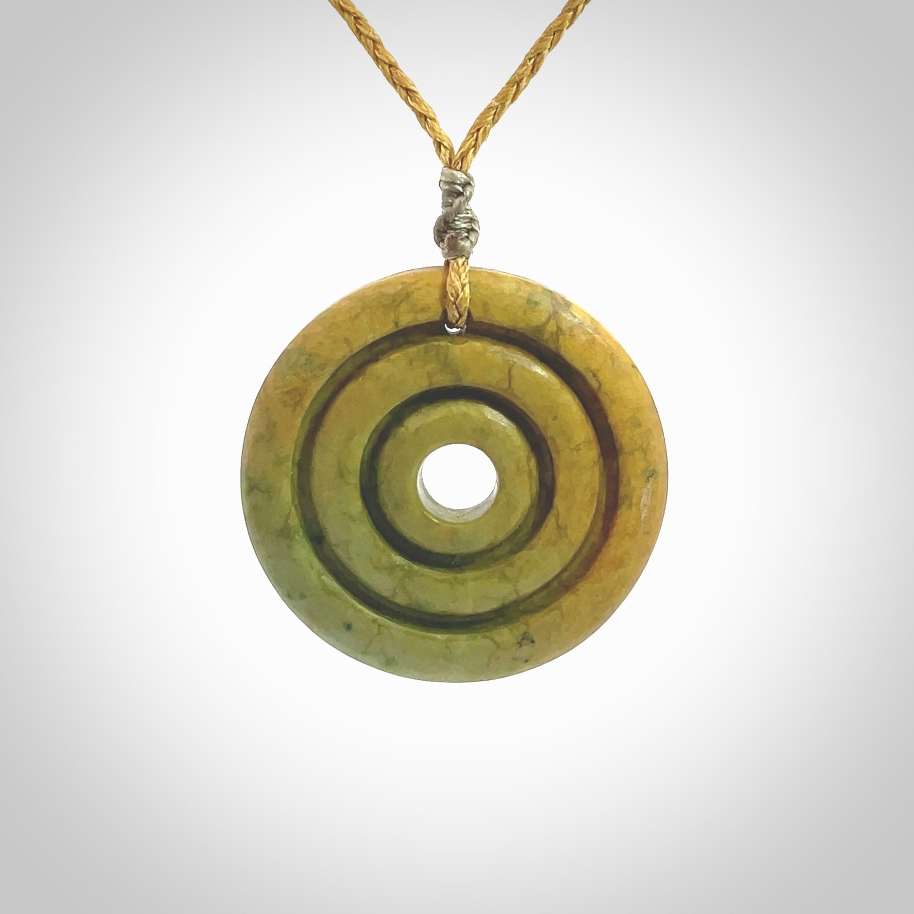 This picture shows a hand carved disc pendant made from a bright orange and green coloured flower jade. The front face is a unique design and the back is flat. It is provided with an adjustable sahara tan cord.