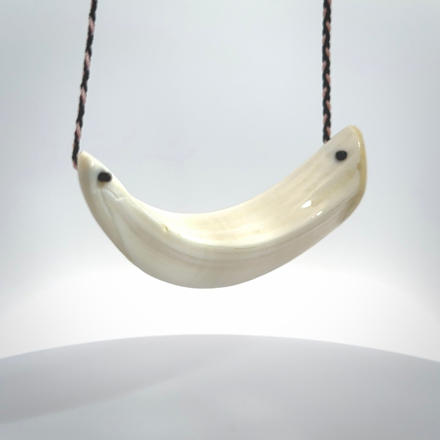 This photo shows a pendant we carved from boars tusk. It is a Blue Whale carved lengthwise into the tusk. This piece is suspended from a hand plaited necklace cord in Black and Pink. This pendant is 100% hand made.