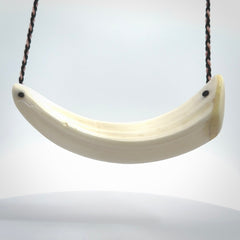 This photo shows a pendant we carved from boars tusk. It is a Blue Whale carved lengthwise into the tusk. This piece is suspended from a hand plaited necklace cord in Black and Pink. This pendant is 100% hand made.