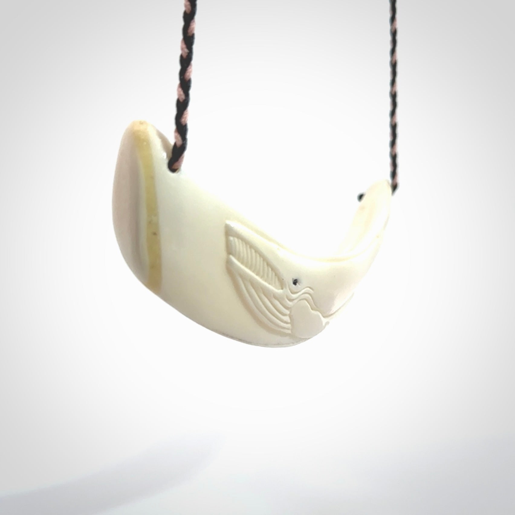 This photo shows a pendant we carved from boars tusk. It is a Blue Whale carved lengthwise into the tusk. This piece is suspended from a hand plaited necklace cord in Black and Pink. This pendant is 100% hand made.