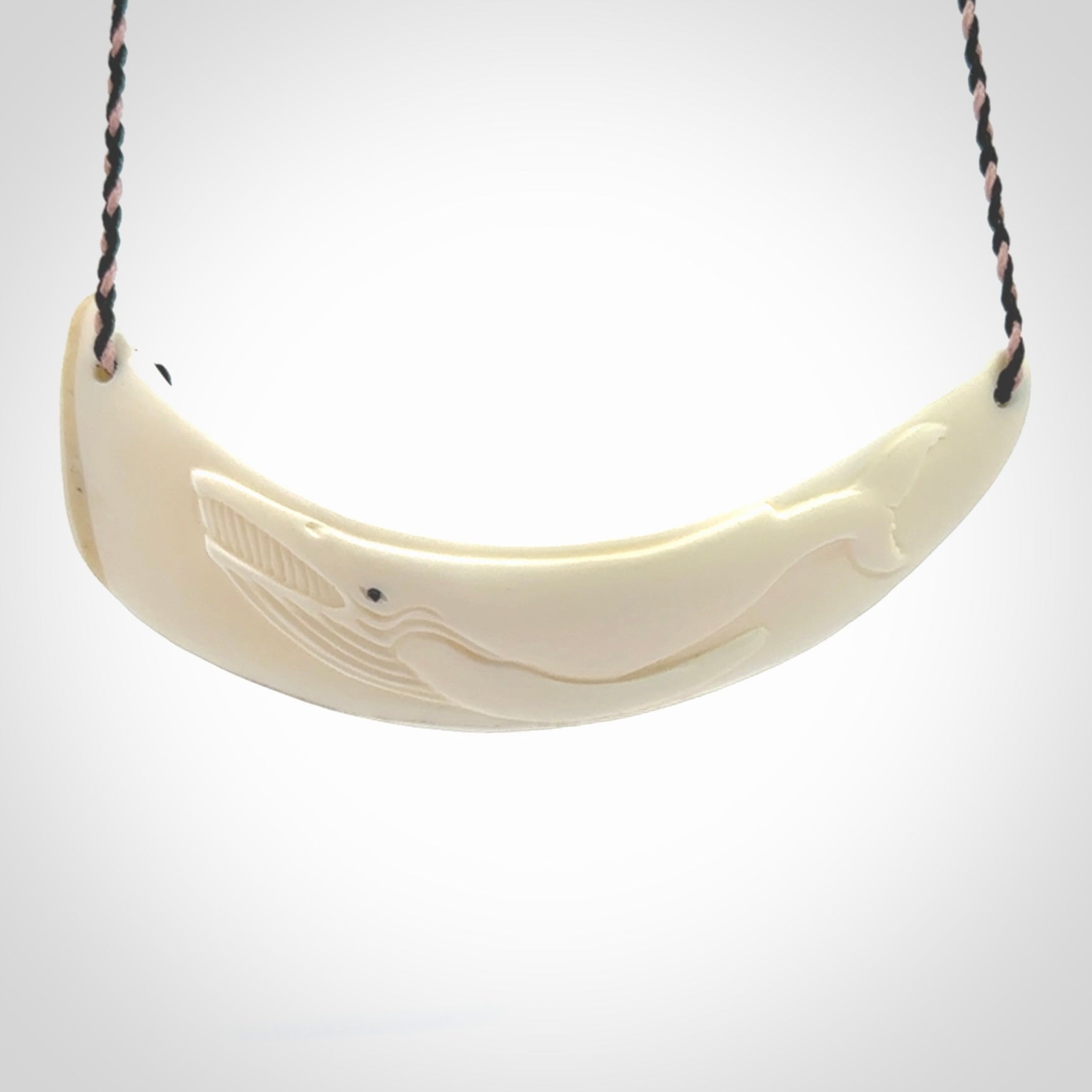 This photo shows a pendant we carved from boars tusk. It is a Blue Whale carved lengthwise into the tusk. This piece is suspended from a hand plaited necklace cord in Black and Pink. This pendant is 100% hand made.