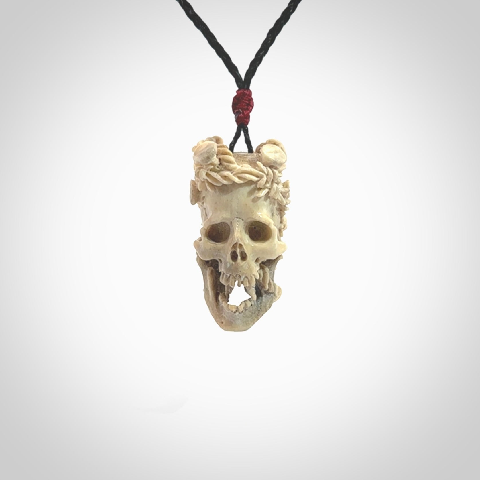 This picture shows a medium sized Deer Antler Bone skull pendant that we have hand carved. It is polished to a soft shine and is a very striking piece. The cord is a black colour and has a small red or grey floret binding just above the pendant.