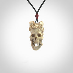 This picture shows a medium sized Deer Antler Bone skull pendant that we have hand carved. It is polished to a soft shine and is a very striking piece. The cord is a black colour and has a small red or grey floret binding just above the pendant.