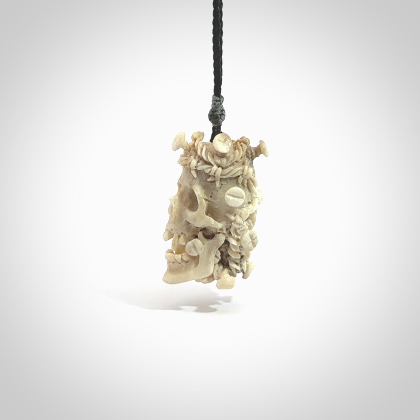 This picture shows a medium sized Deer Antler Bone skull pendant that we have hand carved. It is polished to a soft shine and is a very striking piece. The cord is a black colour and has a small red or grey floret binding just above the pendant.