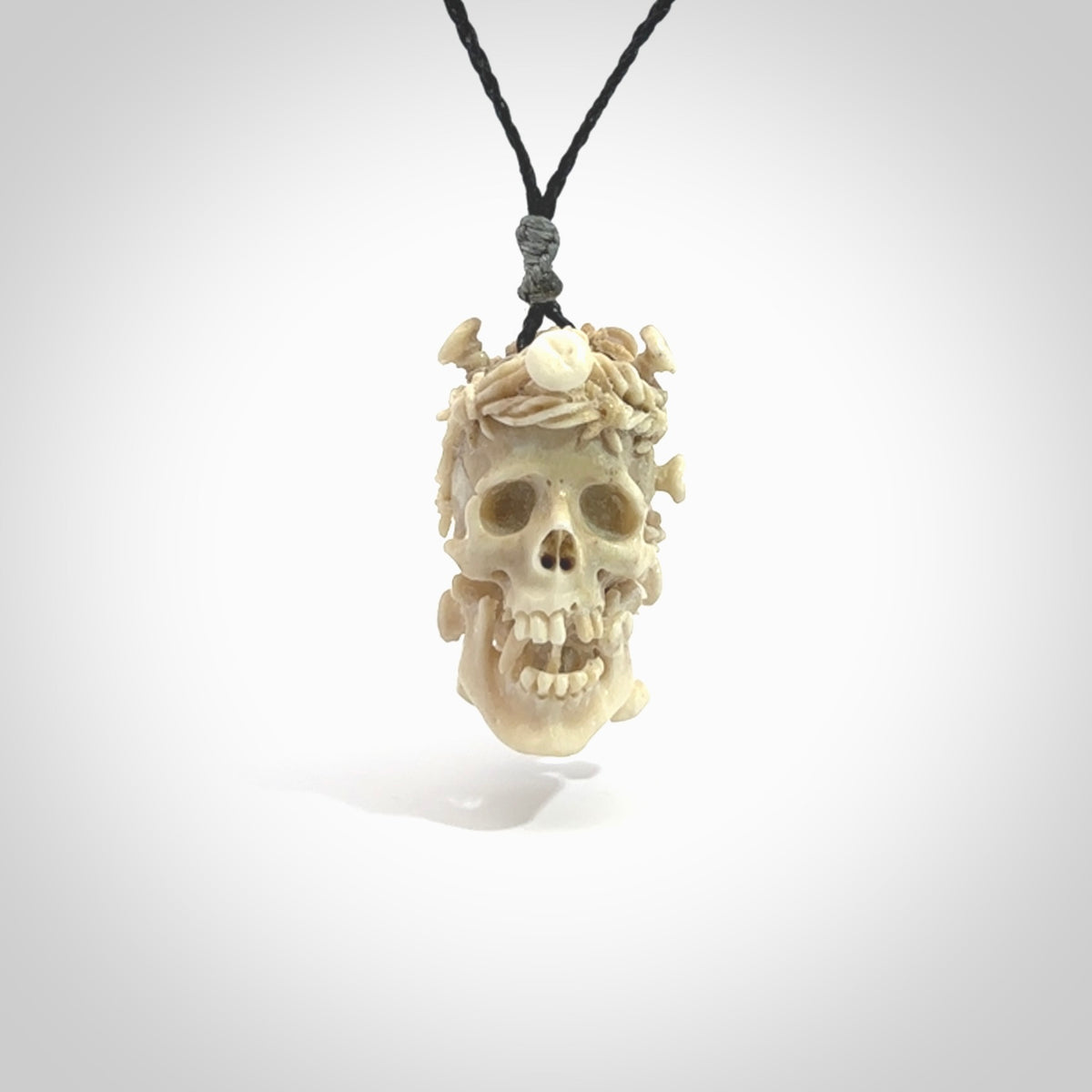 This picture shows a medium sized Deer Antler Bone skull pendant that we have hand carved. It is polished to a soft shine and is a very striking piece. The cord is a black colour and has a small red or grey floret binding just above the pendant.