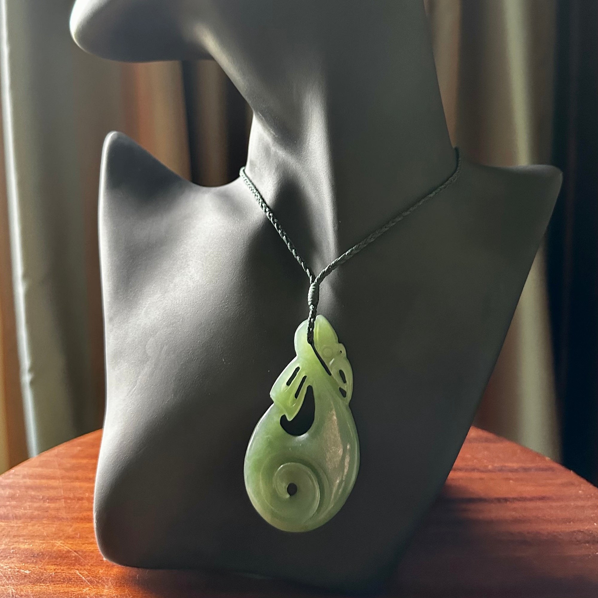 Hand carved New Zealand Inanga jade manaia with koru pendant. Carved from beautiful New Zealand Jade for NZ Pacific by Ross Crump. Unique jade jewellery for sale online. Provided with an adjustable manuka green cord.