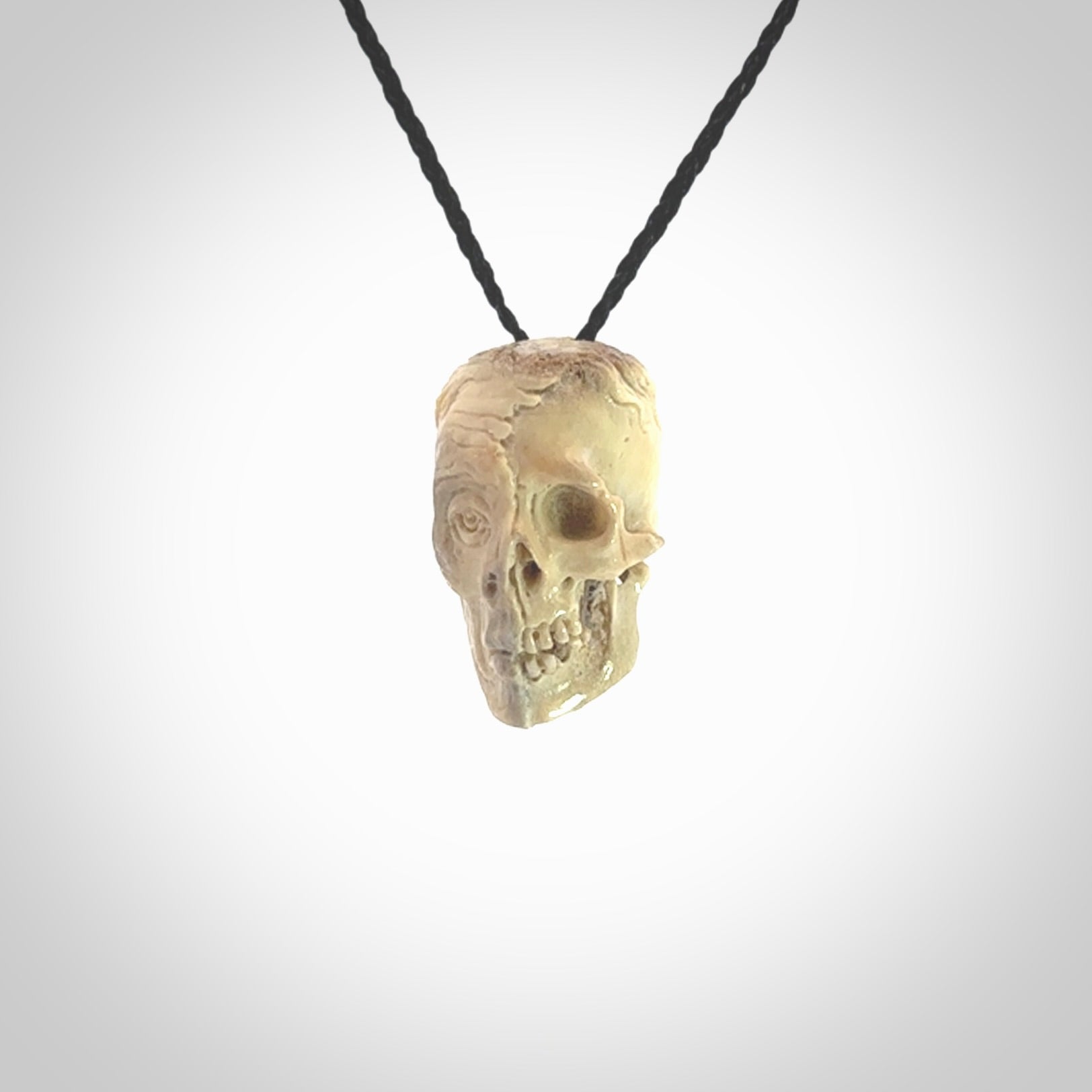 This photo shows a mummy skull pendant hand carved in deer antler. It is provided with a plaited cord necklace which is length adjustable.