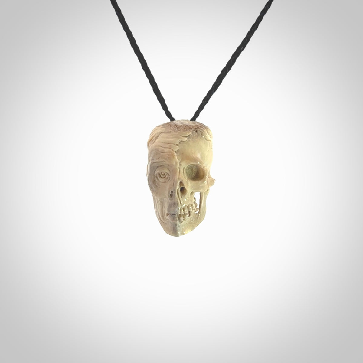 This photo shows a mummy skull pendant hand carved in deer antler. It is provided with a plaited cord necklace which is length adjustable.