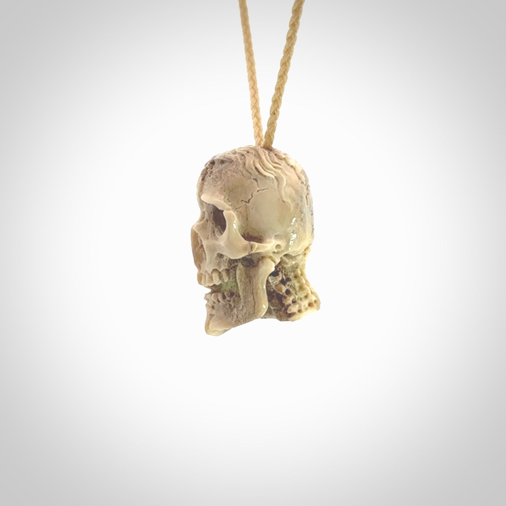 This photo shows a mummy skull pendant hand carved in deer antler. It is provided with a plaited cord necklace which is length adjustable.