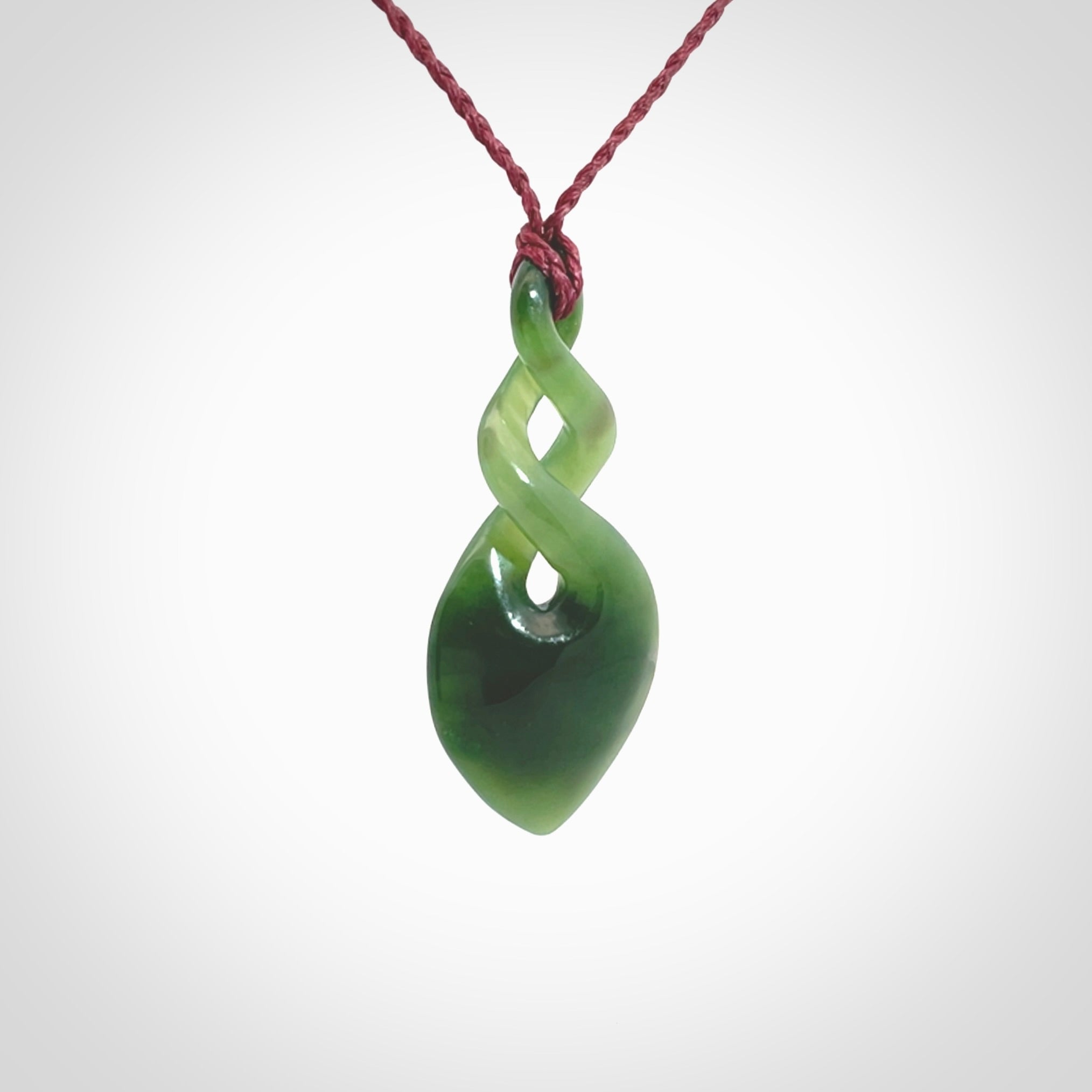 Hand carved New Zealand jade twist pendant. Carved in New Zealand by NZ Pacific. Unique double twist jewellery for sale online. Provided with an adjustable Burgundy cord.