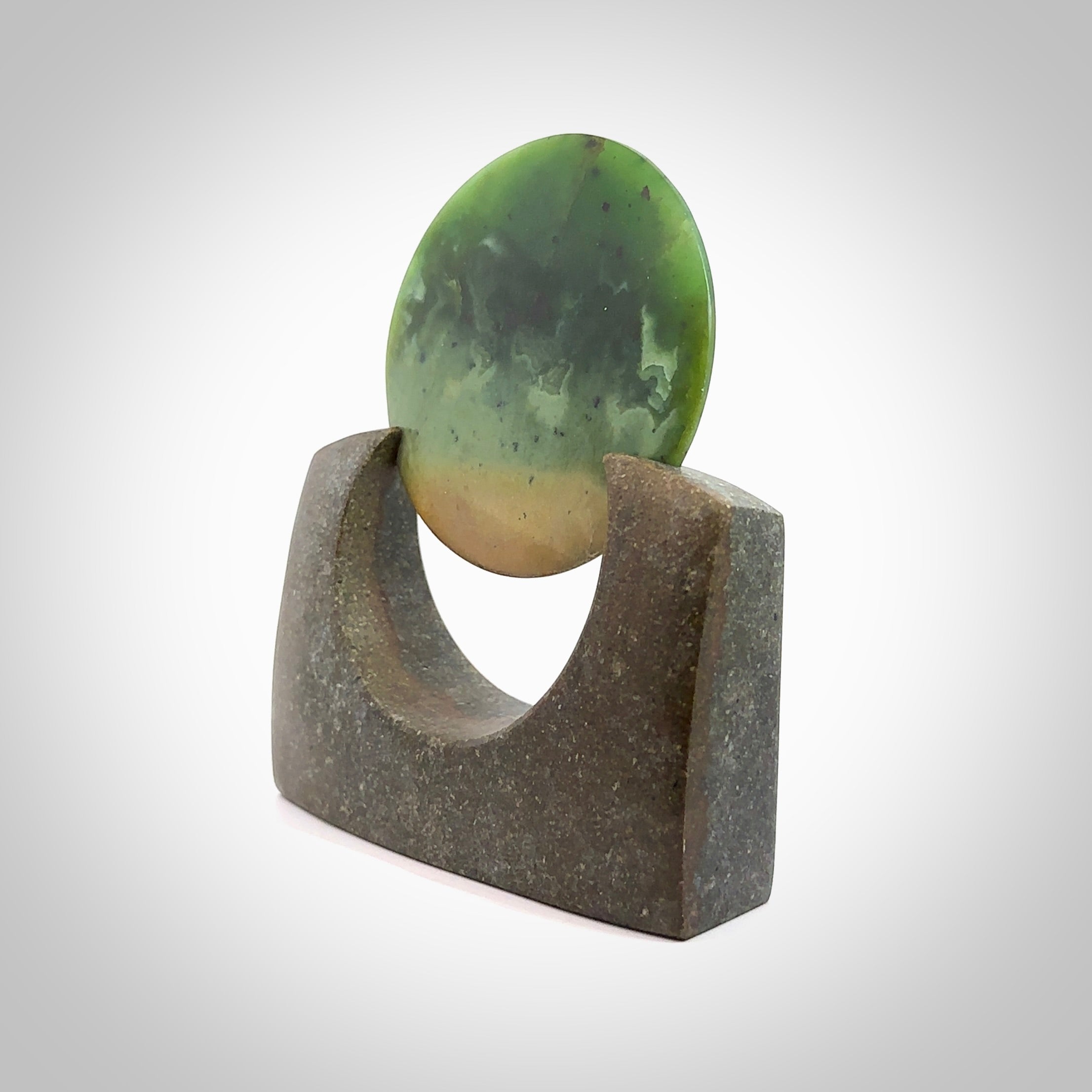 Hand carved New Zealand Flower Jade Disc with Greywacke stand sculpture. Hand carved here in New Zealand by Ric Moor. This is a 'one only' sculpture, a beautiful display piece. Small Jade disc sculpture for desk.