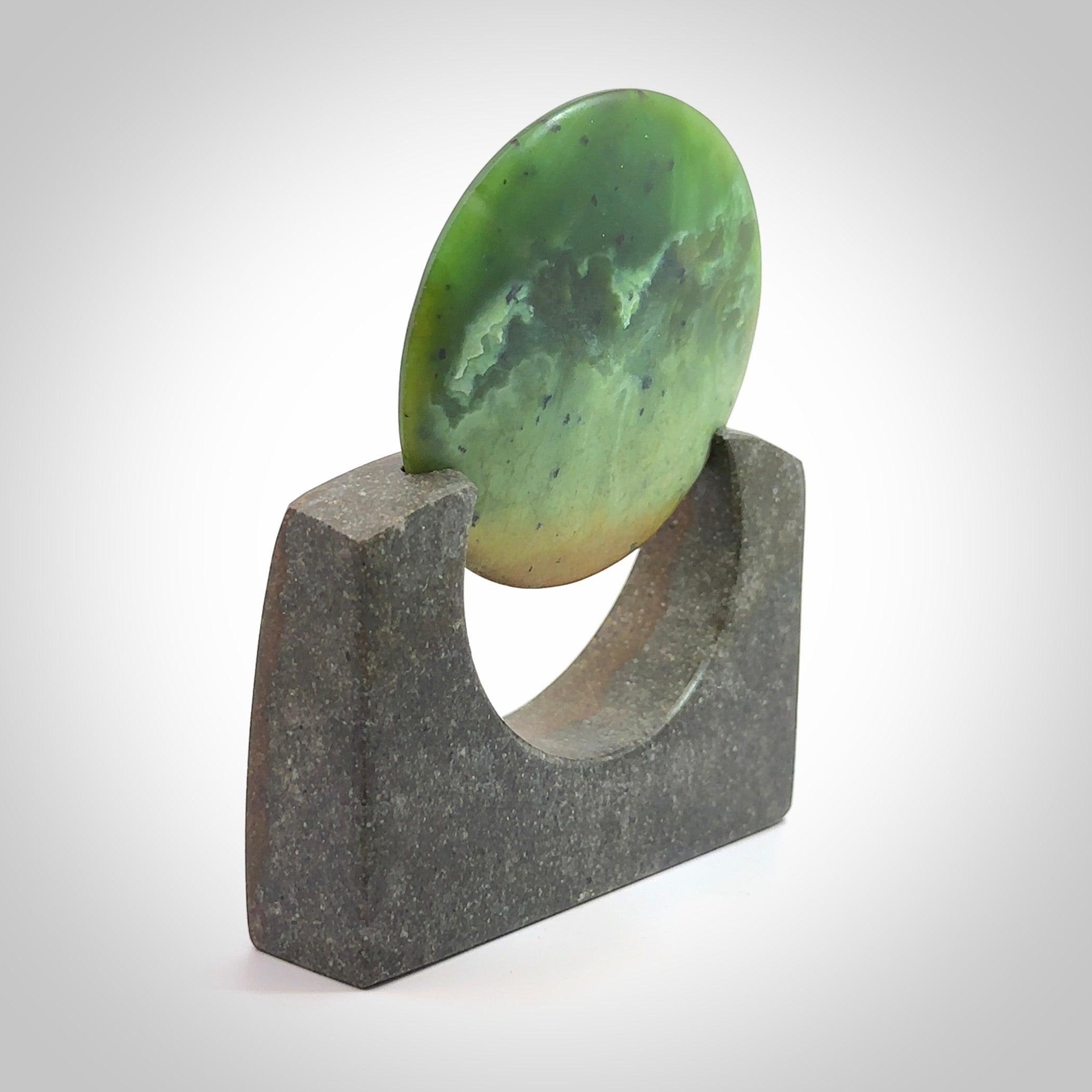 Hand carved New Zealand Flower Jade Disc with Greywacke stand sculpture. Hand carved here in New Zealand by Ric Moor. This is a 'one only' sculpture, a beautiful display piece. Small Jade disc sculpture for desk.