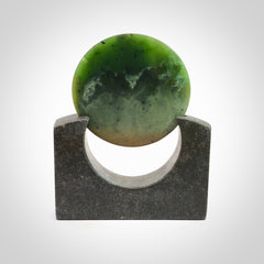 Hand carved New Zealand Flower Jade Disc with Greywacke stand sculpture. Hand carved here in New Zealand by Ric Moor. This is a 'one only' sculpture, a beautiful display piece. Small Jade disc sculpture for desk.