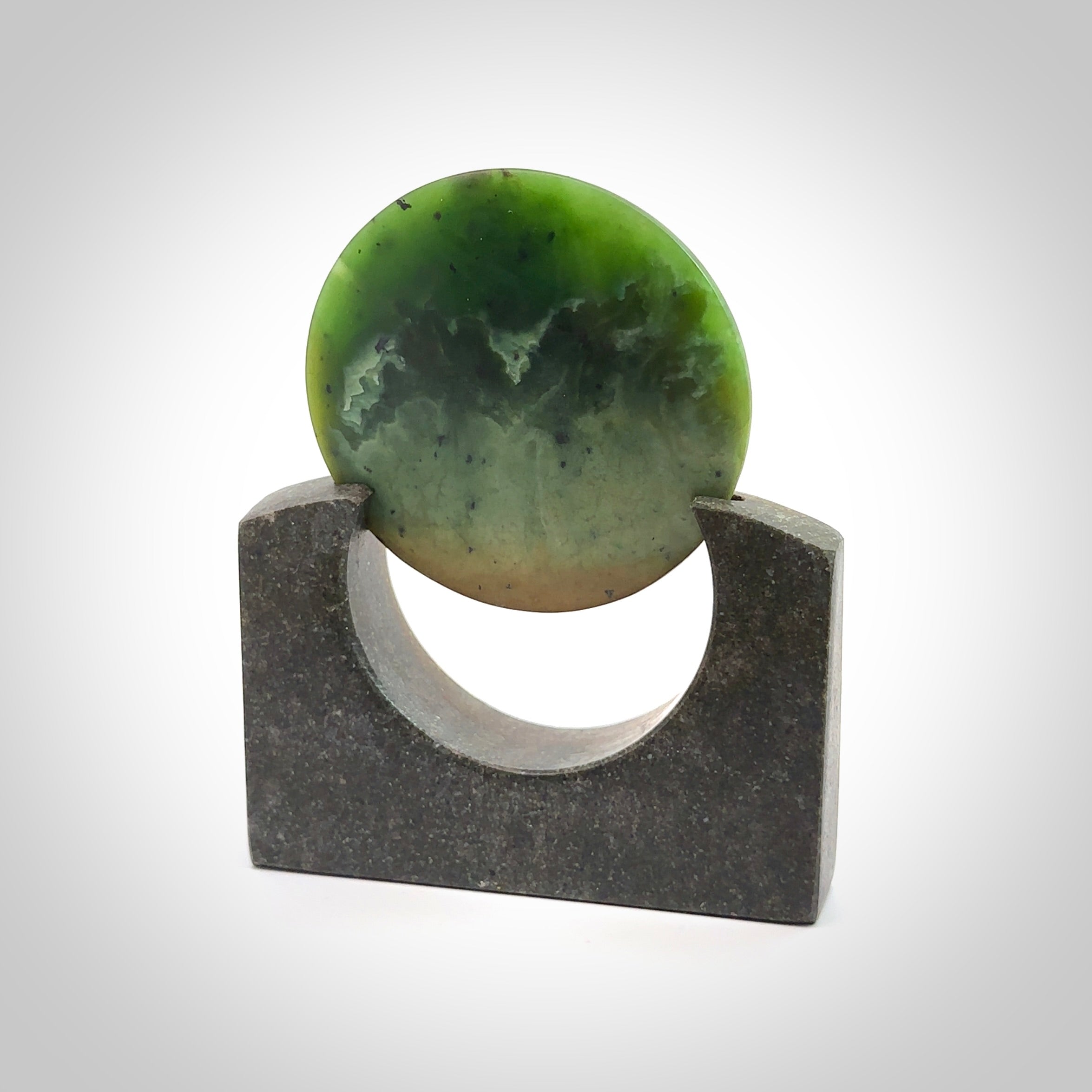 Hand carved New Zealand Flower Jade Disc with Greywacke stand sculpture. Hand carved here in New Zealand by Ric Moor. This is a 'one only' sculpture, a beautiful display piece. Small Jade disc sculpture for desk.